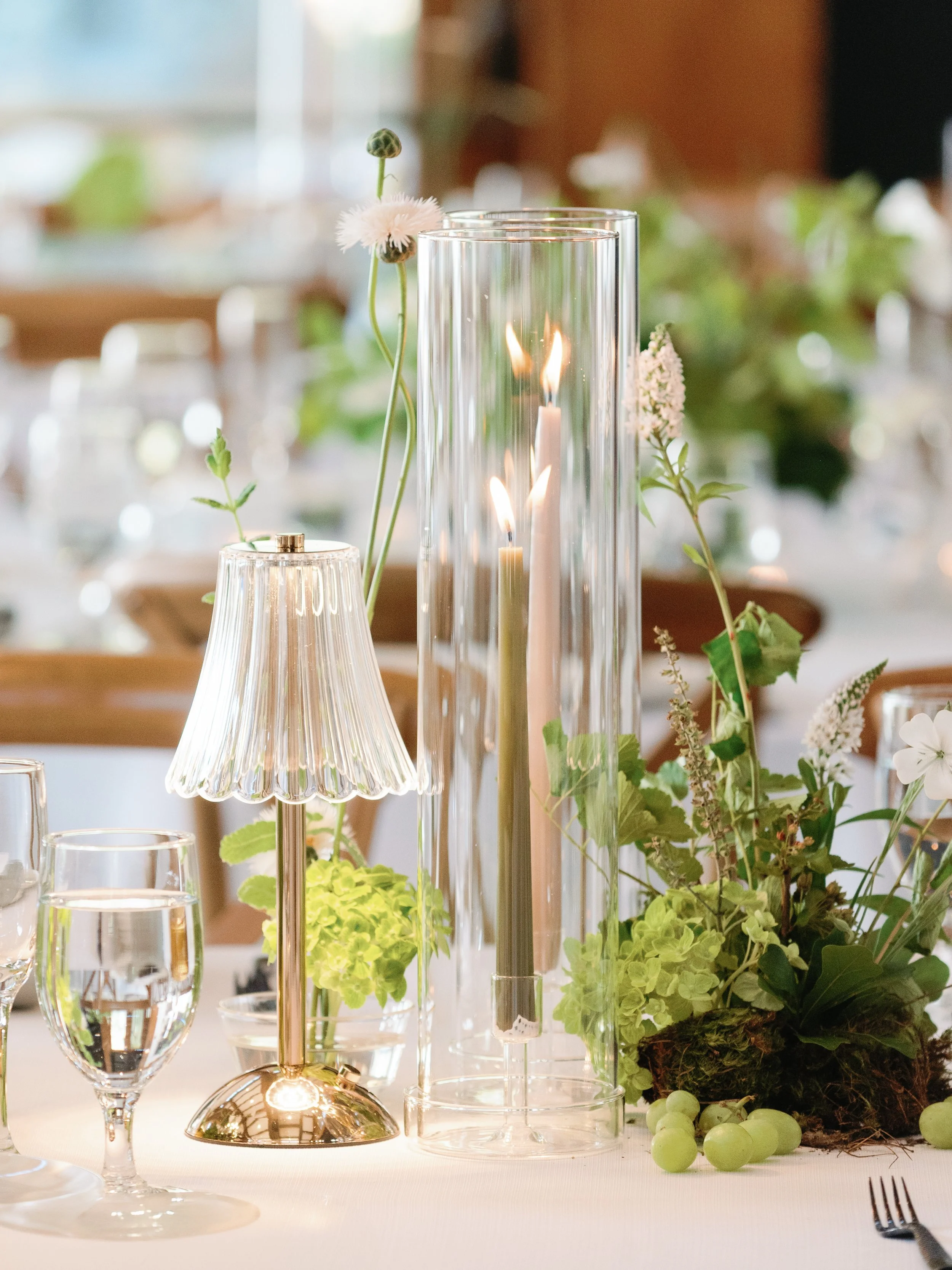 A table centerpiece with candles, flowers, and greenery at an event or restaurant.