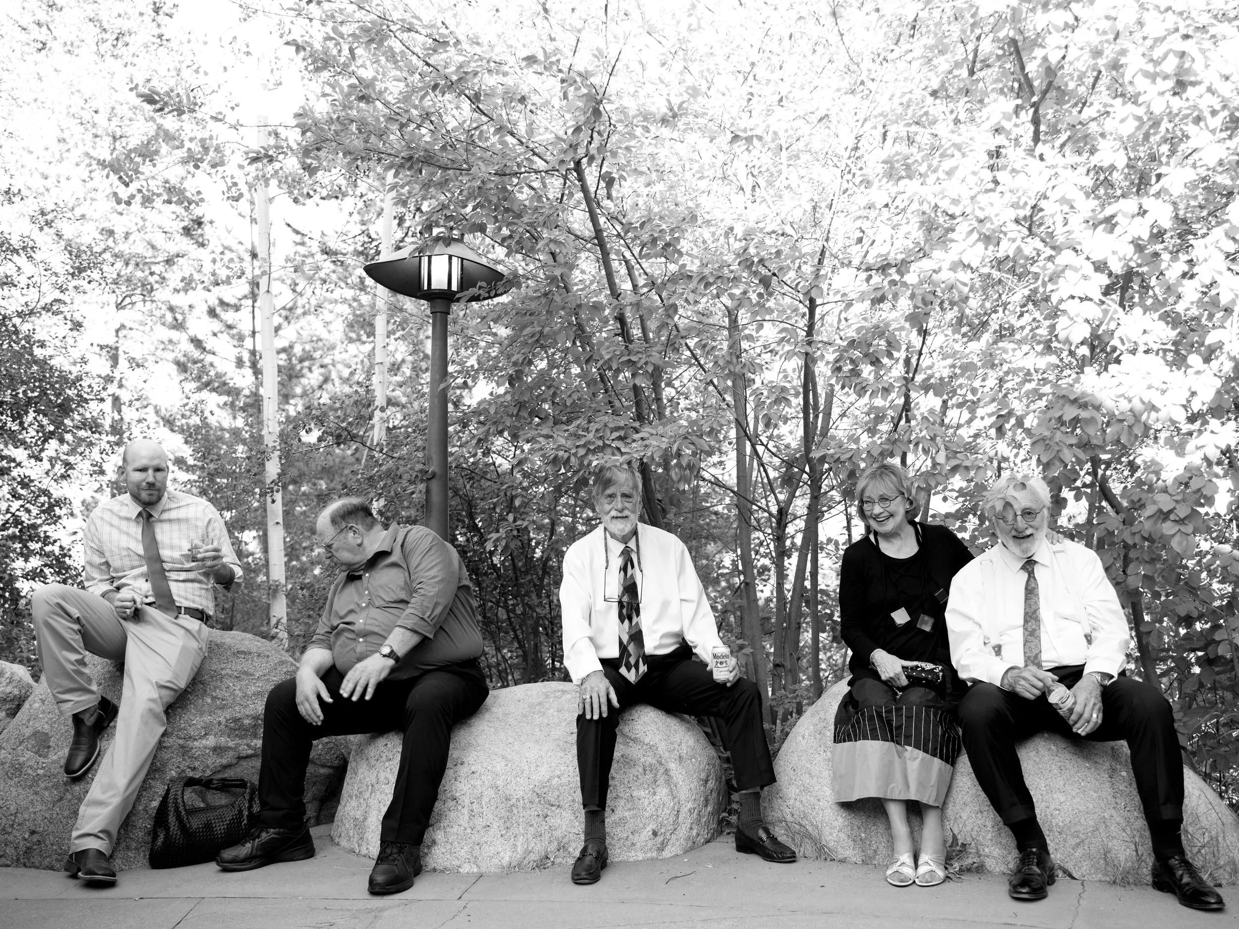 Five people sitting on large rocks outdoors, with trees and a lamppost in the background.