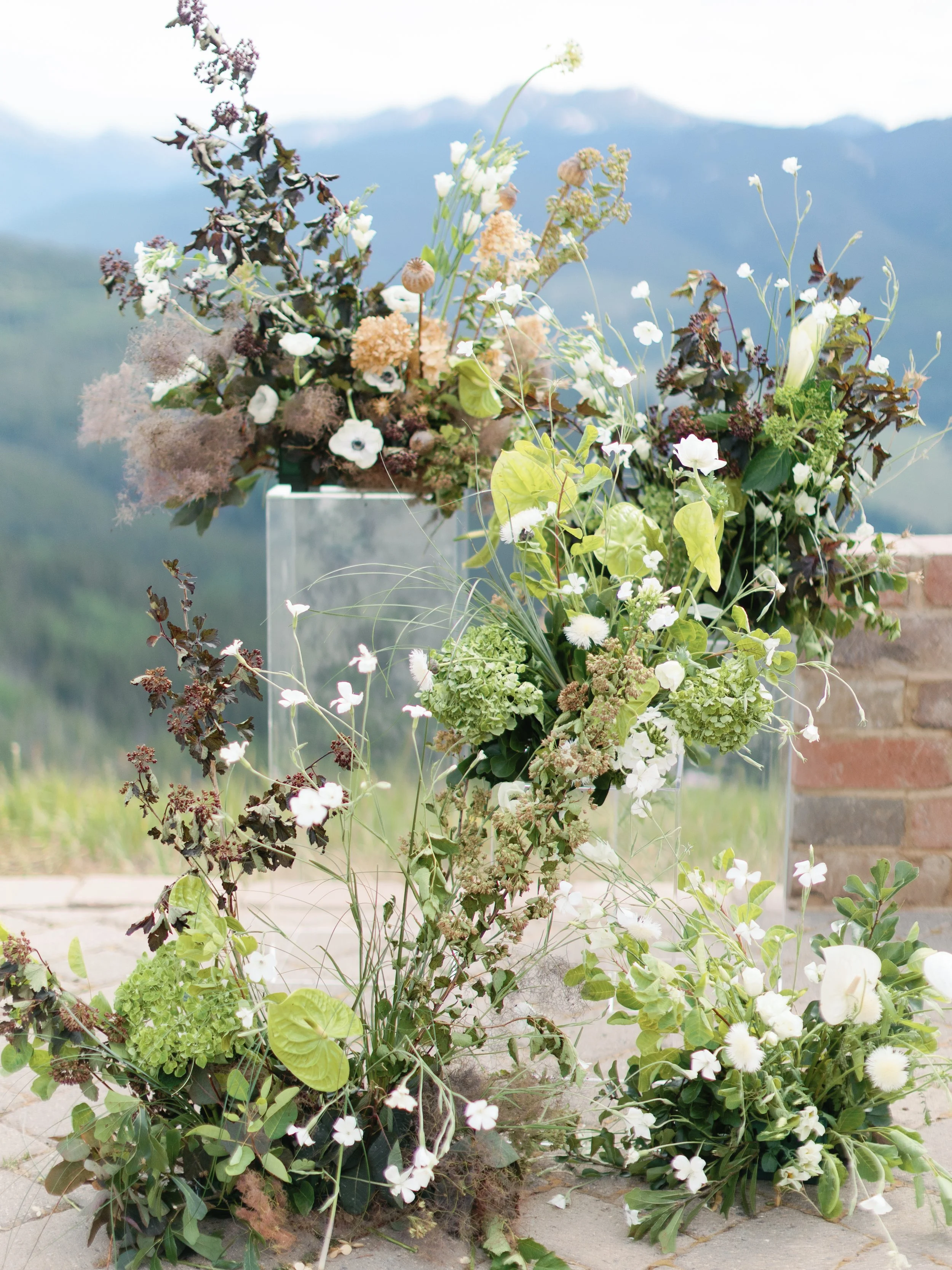Various white and green flowers arranged outdoors with mountainous background.