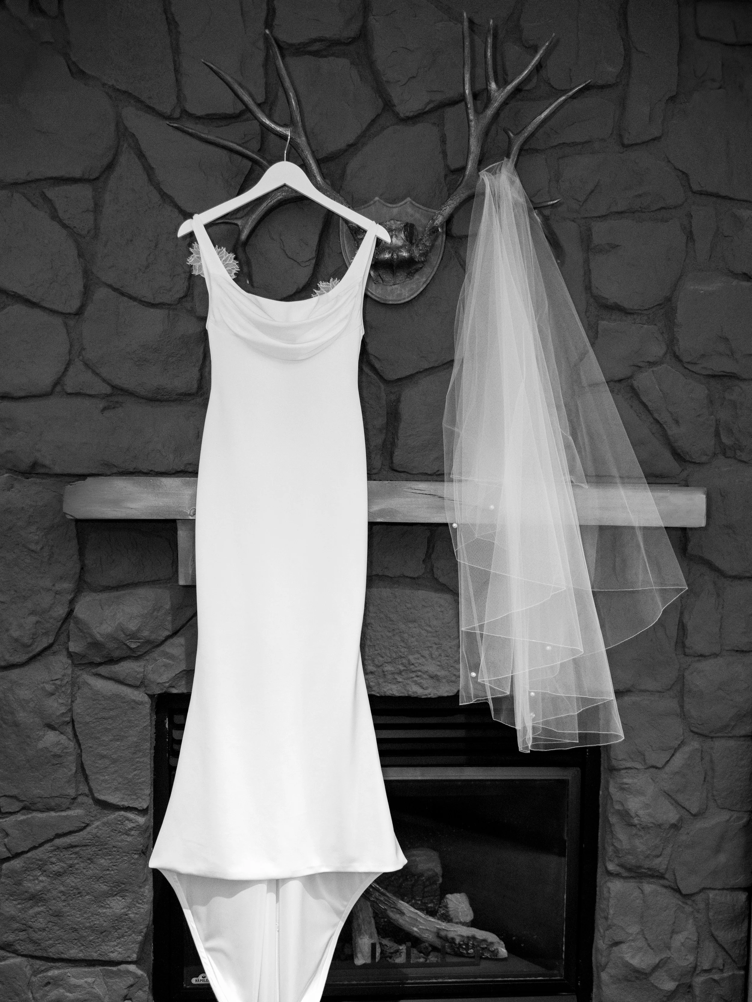 A wedding dress and veil hanging on a decorative antler wall mount above a fireplace.