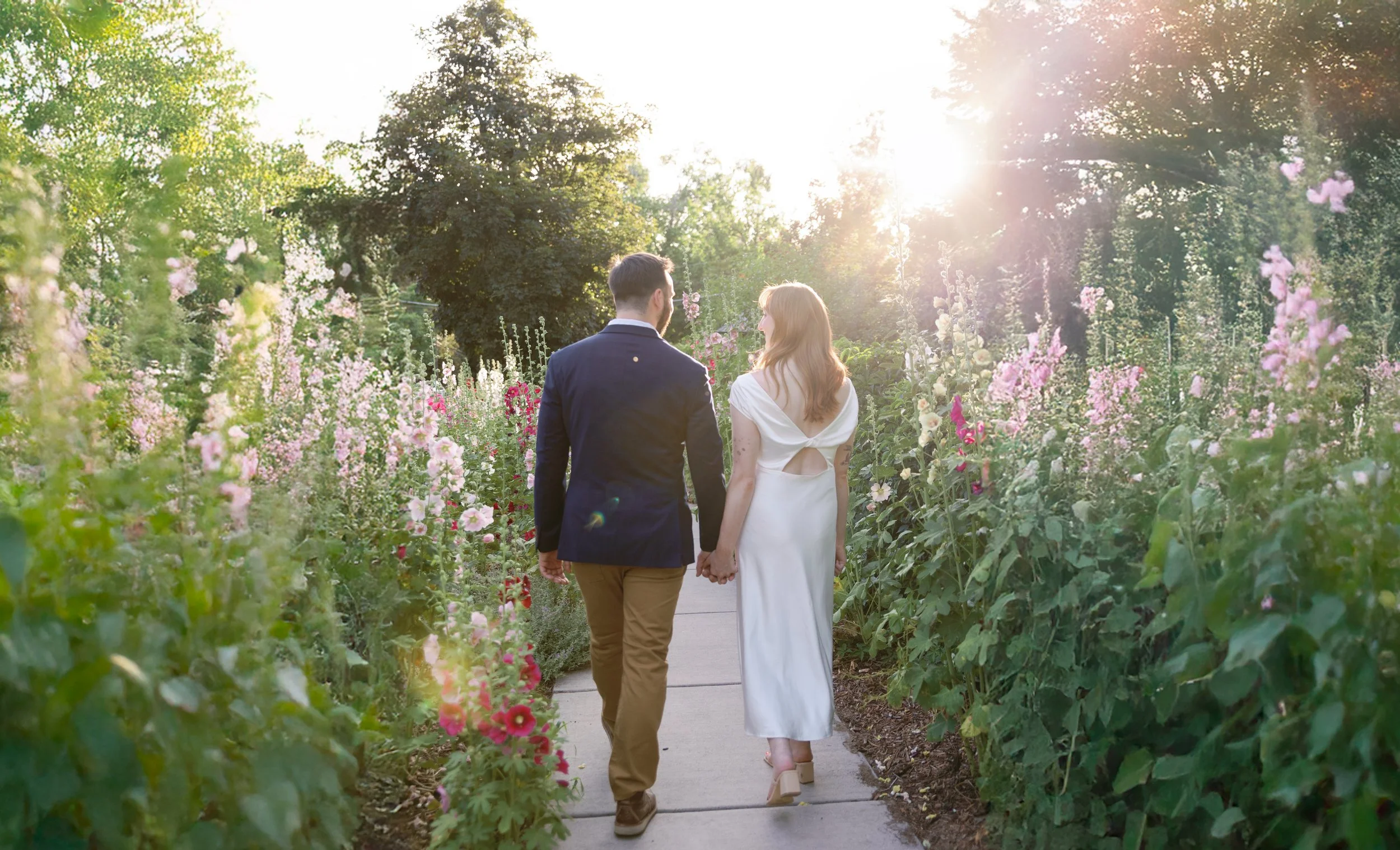 A couple walking hand in hand through a garden with blooming flowers at sunset.