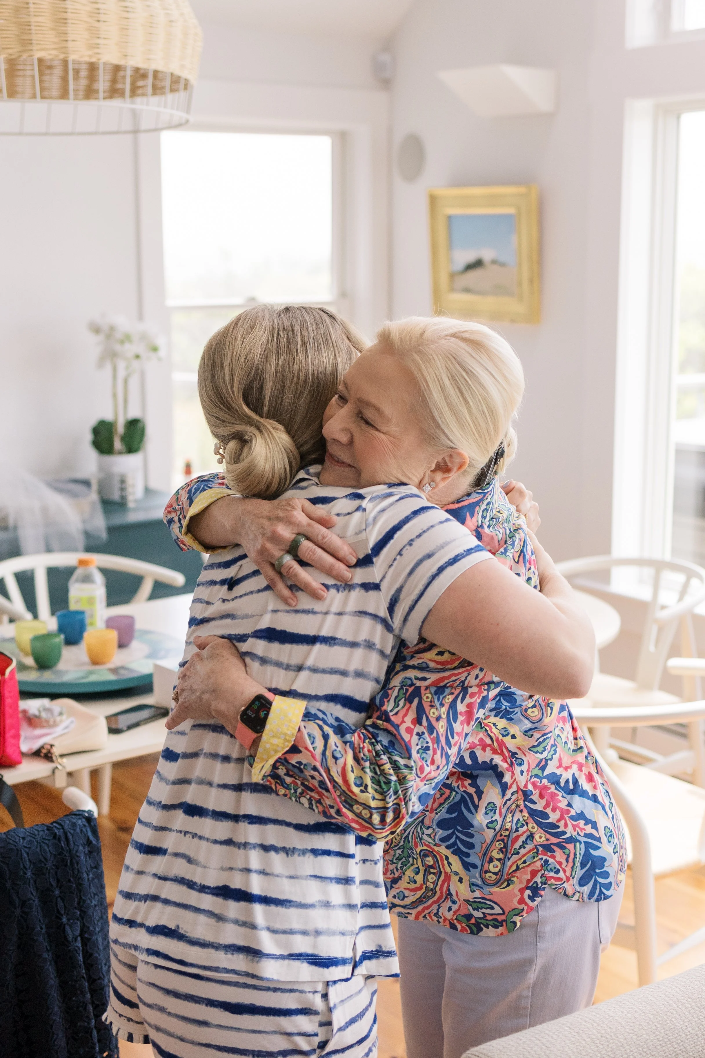 Two women hugging each other warmly in a bright, cozy room with modern decor.