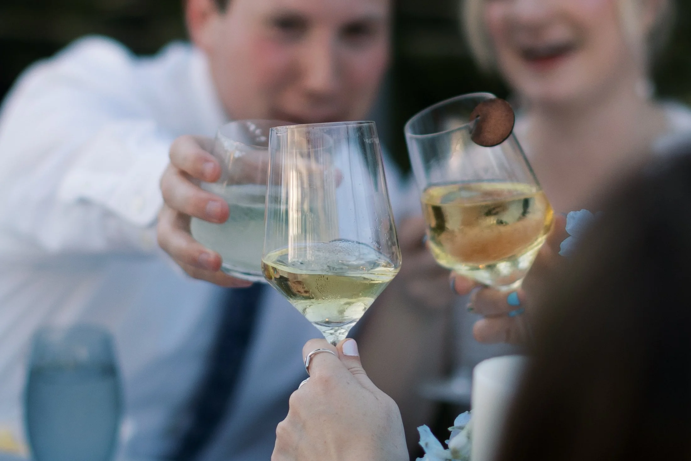 Three people raising glasses of white wine for a toast at a celebration.