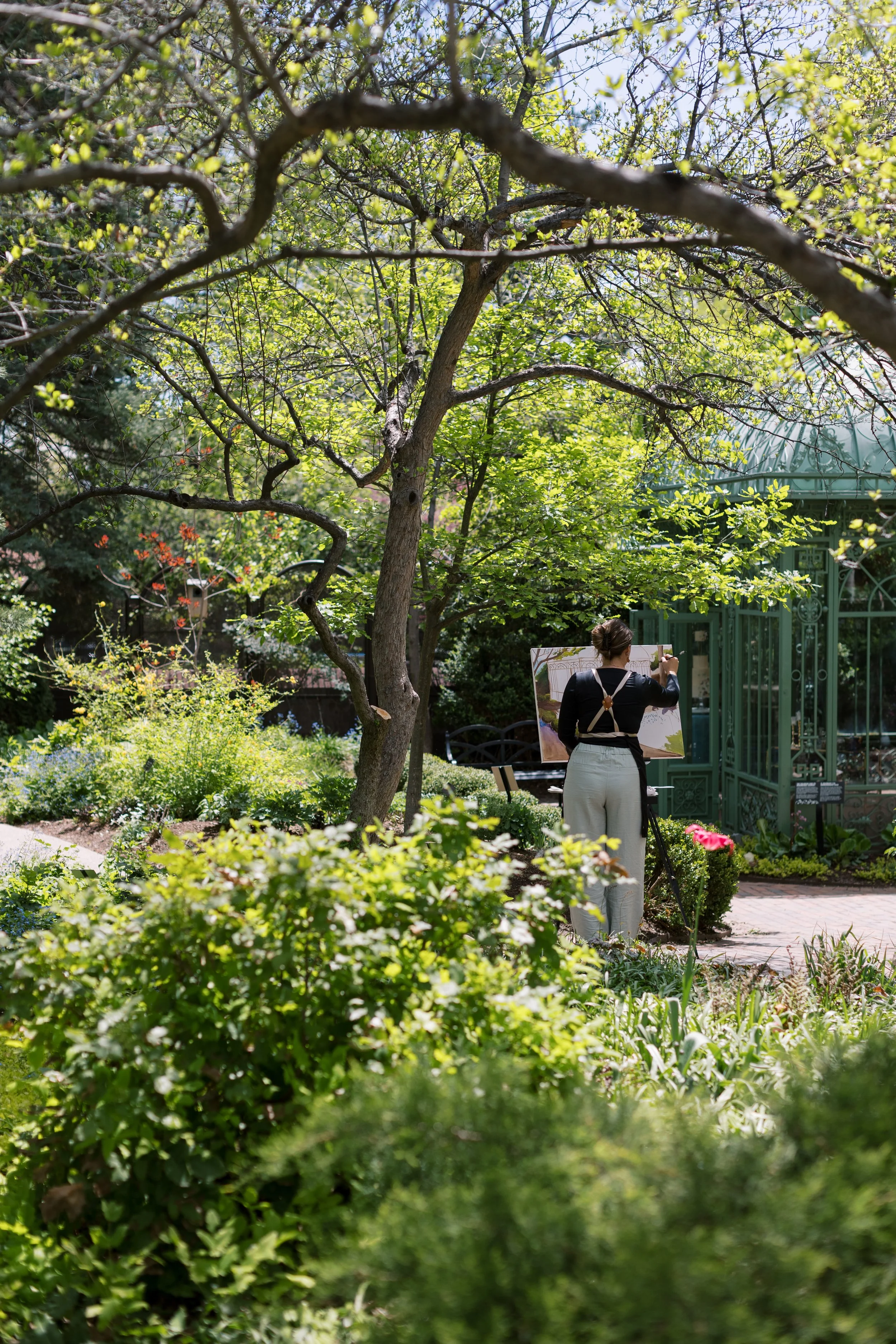 A woman painting outdoors in a lush, green garden.