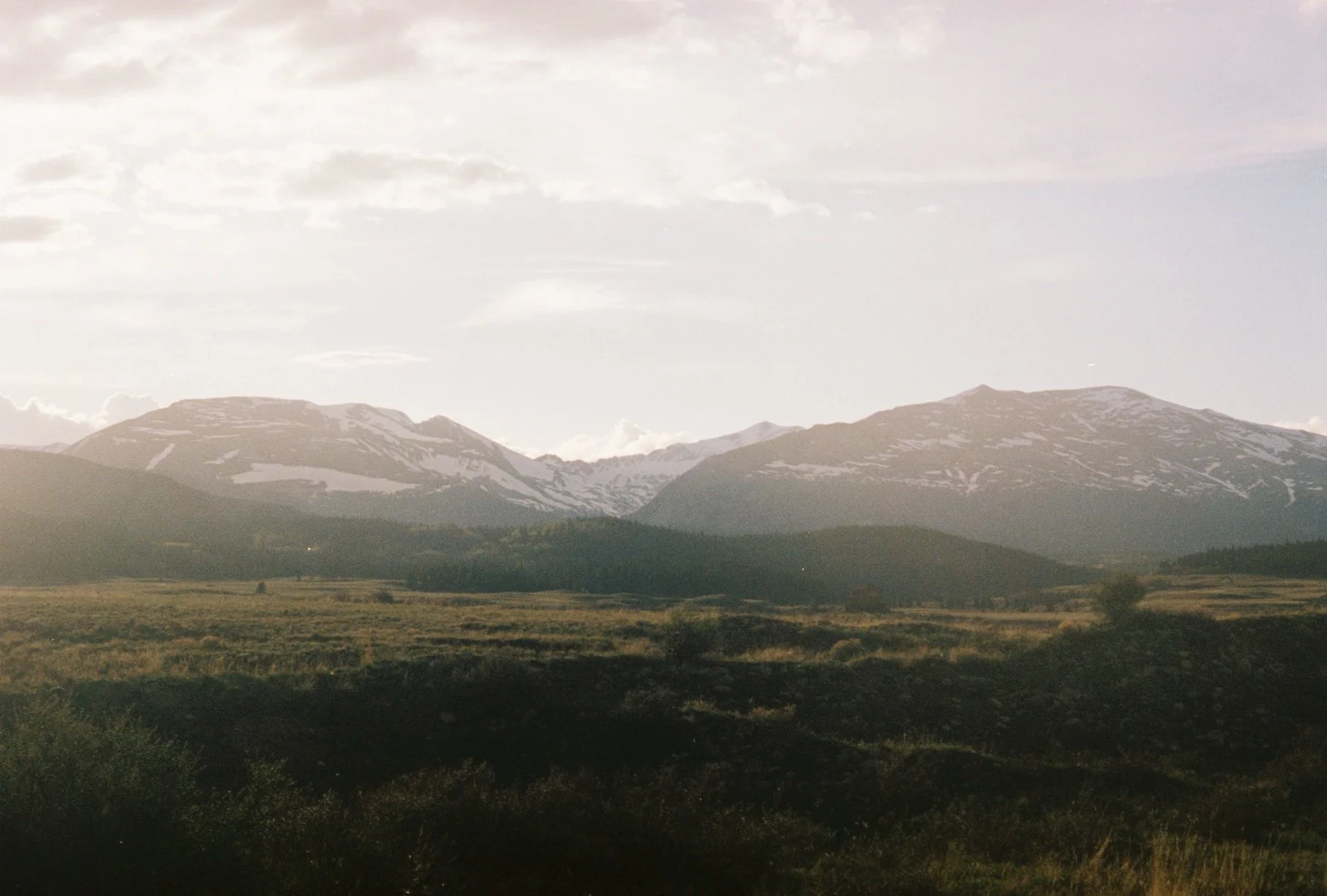 Mountain landscape with snow-capped peaks in the distance and grassy plains in the foreground.
