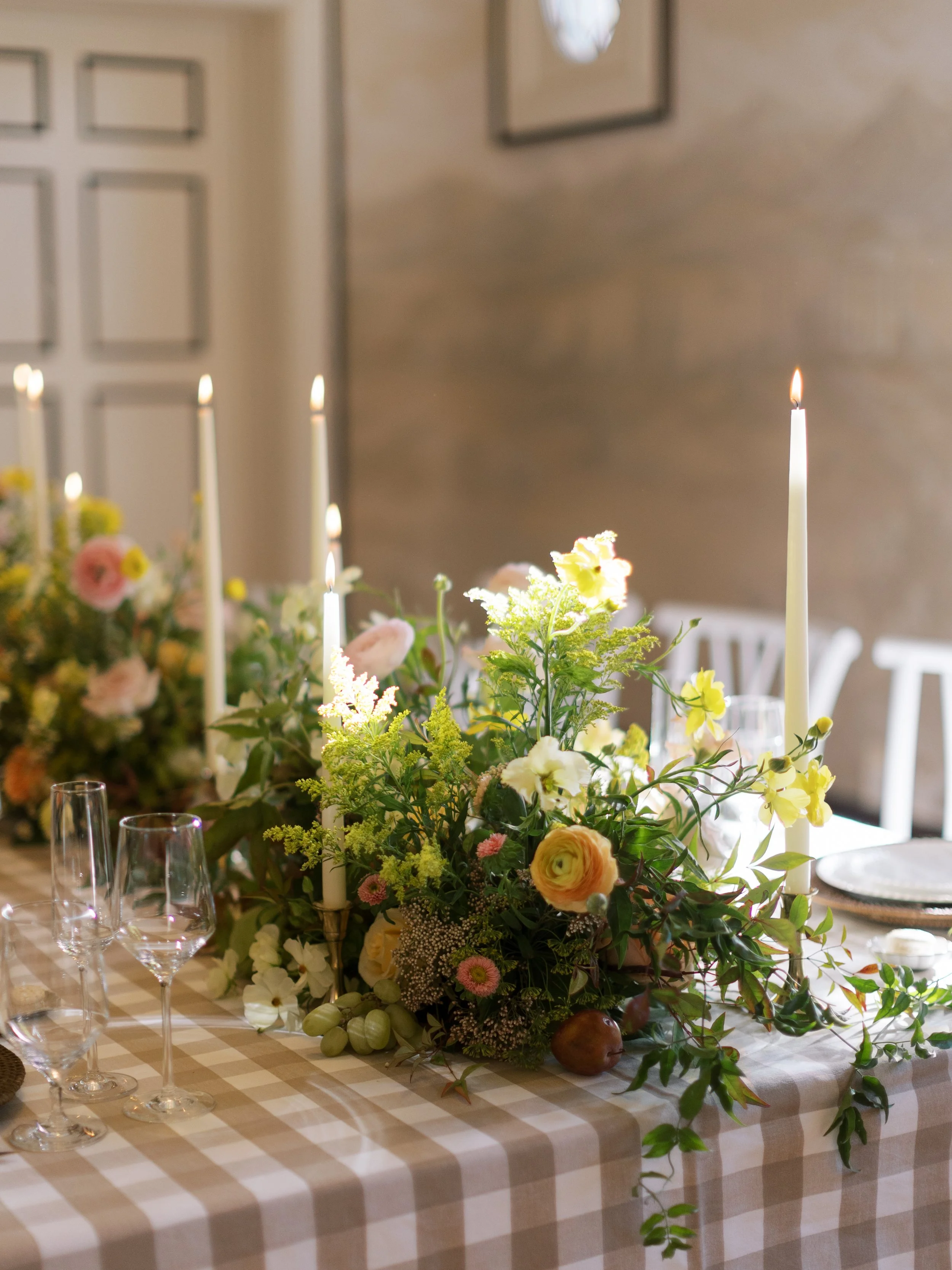 A floral centerpiece with candles on a checkered tablecloth at a decorated dining table.