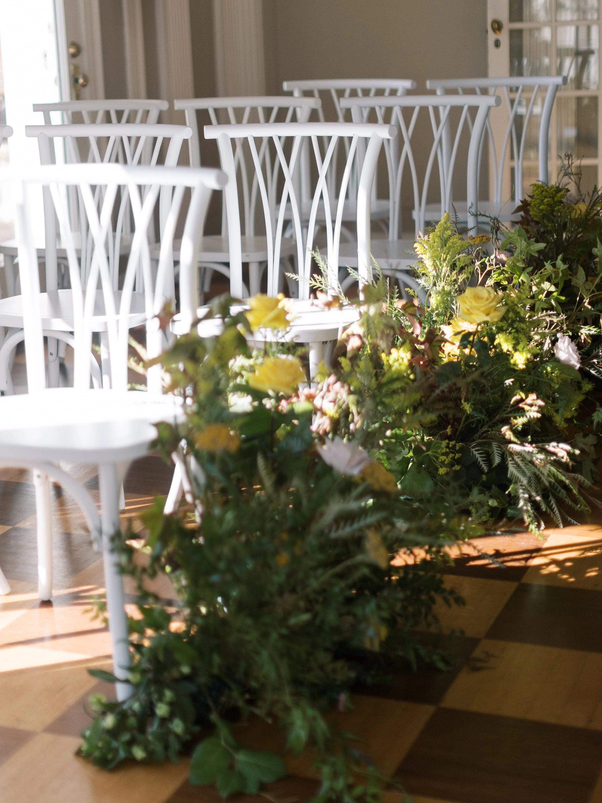Indoor dining area with white chairs arranged at a table decorated with green plants and yellow flowers