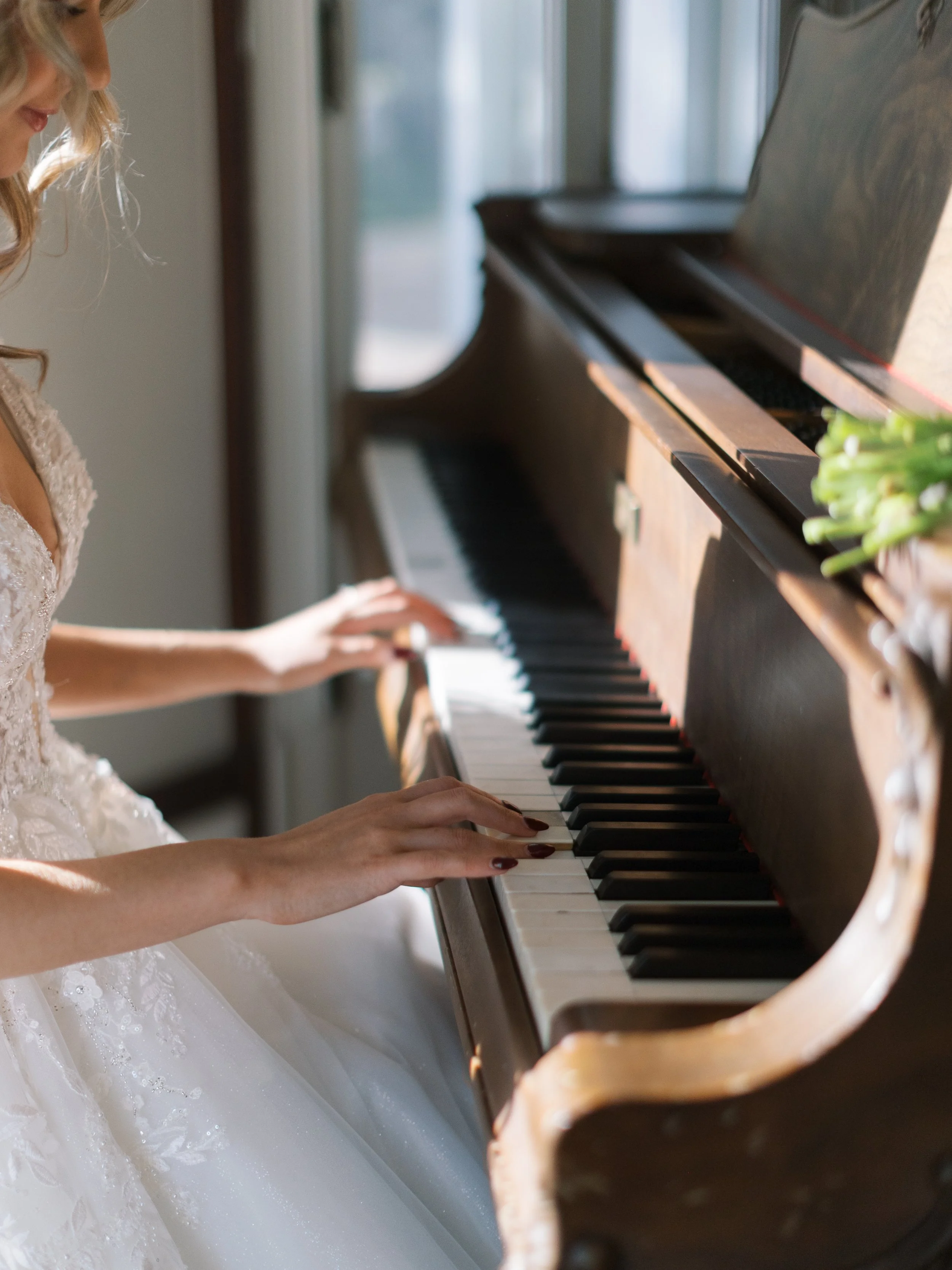 A woman in a white wedding dress playing a grand piano with a wooden finish.