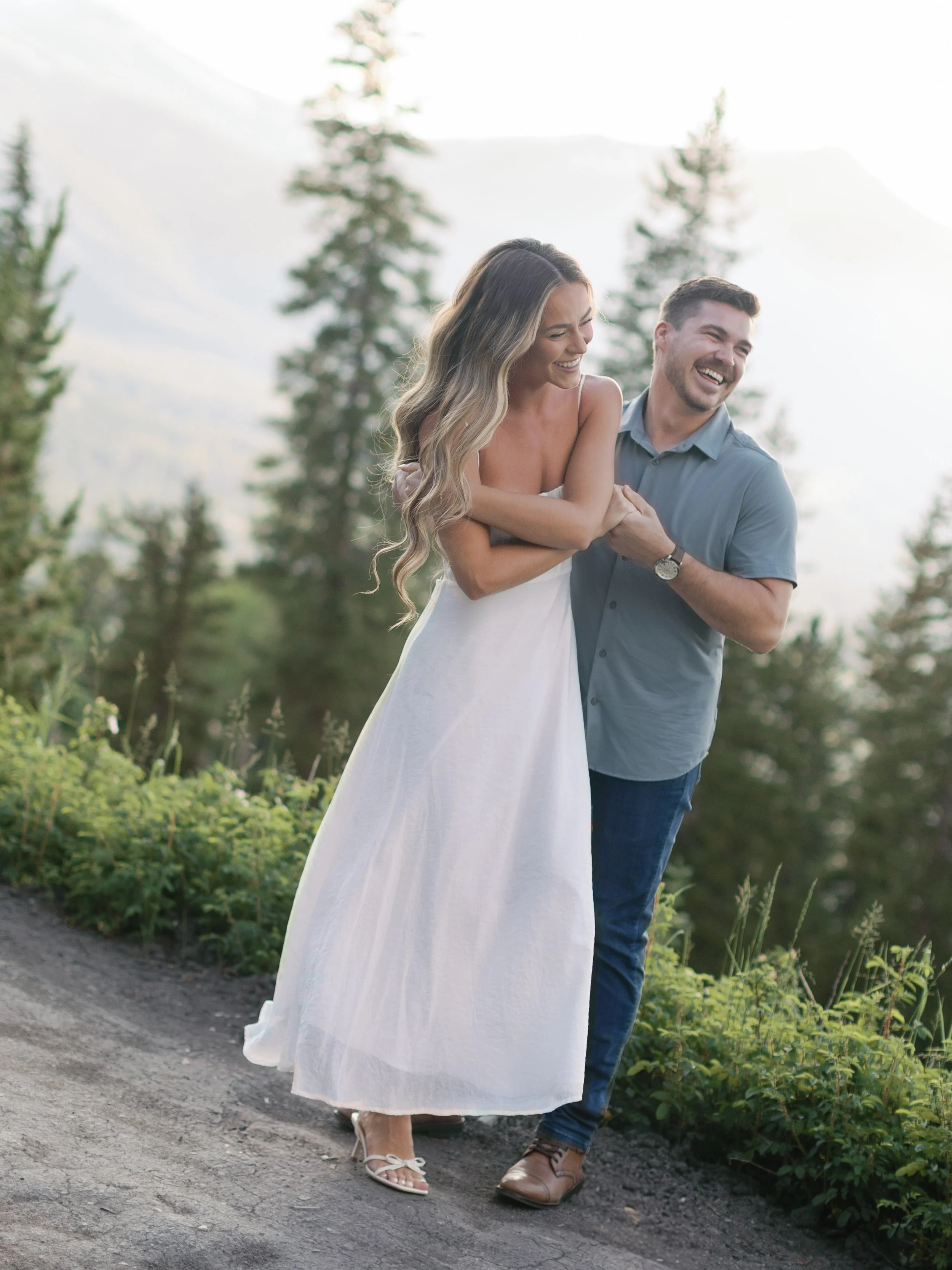 A couple is laughing and walking together outdoors in a mountainous area.
