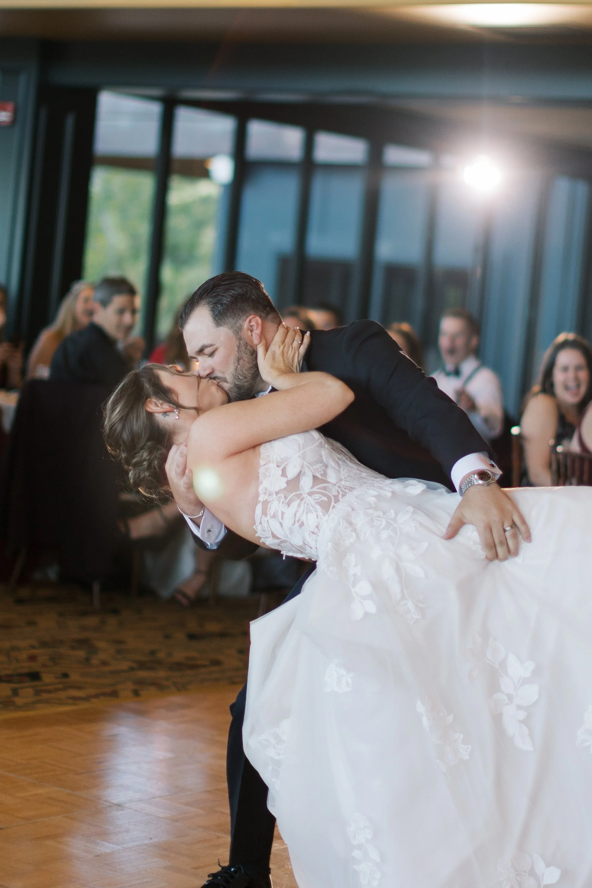 A bride and groom sharing a kiss while dancing at their wedding reception, with guests watching and smiling in the background.