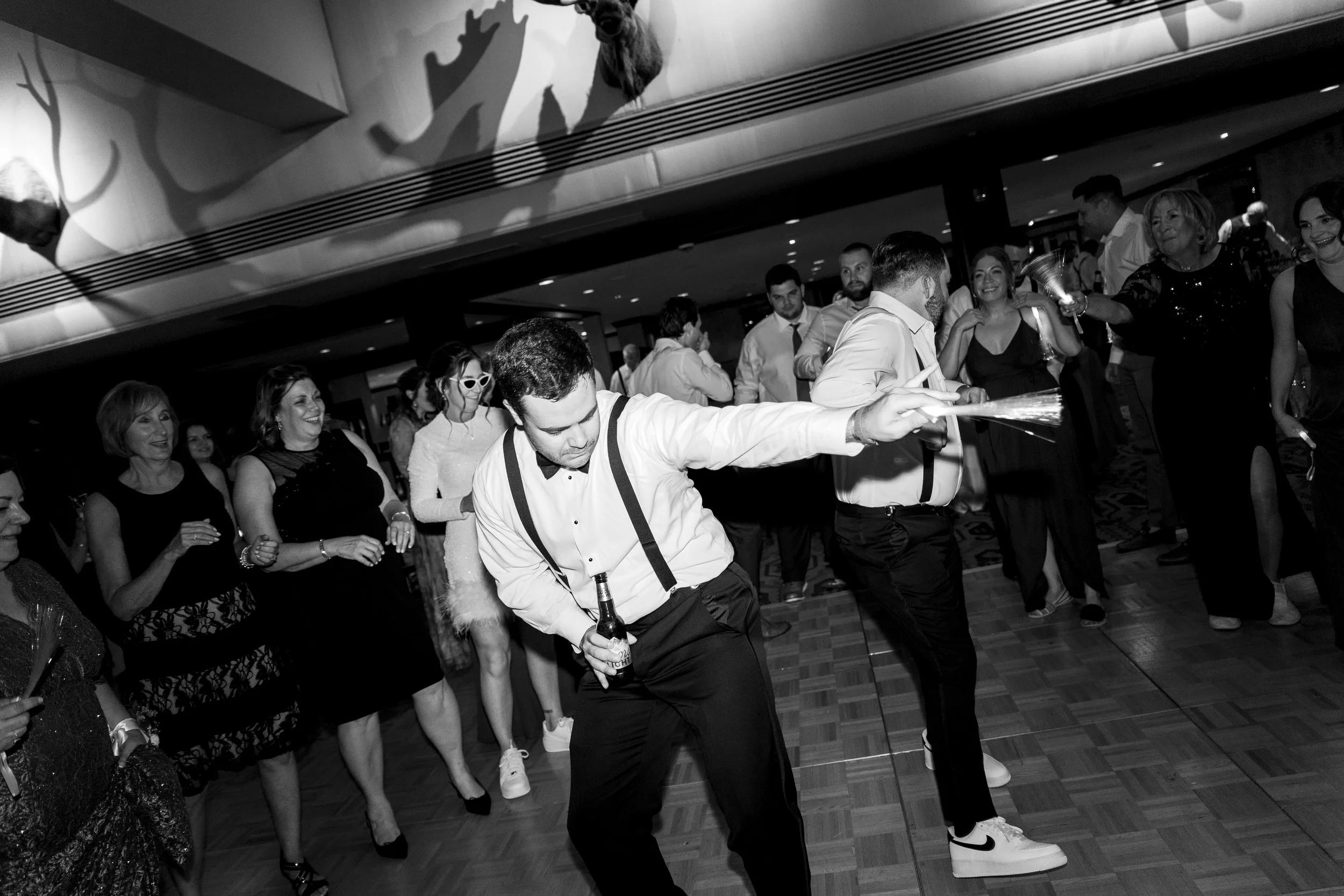 People dancing and celebrating at a party, some are holding drinks, in a decorated event space.
