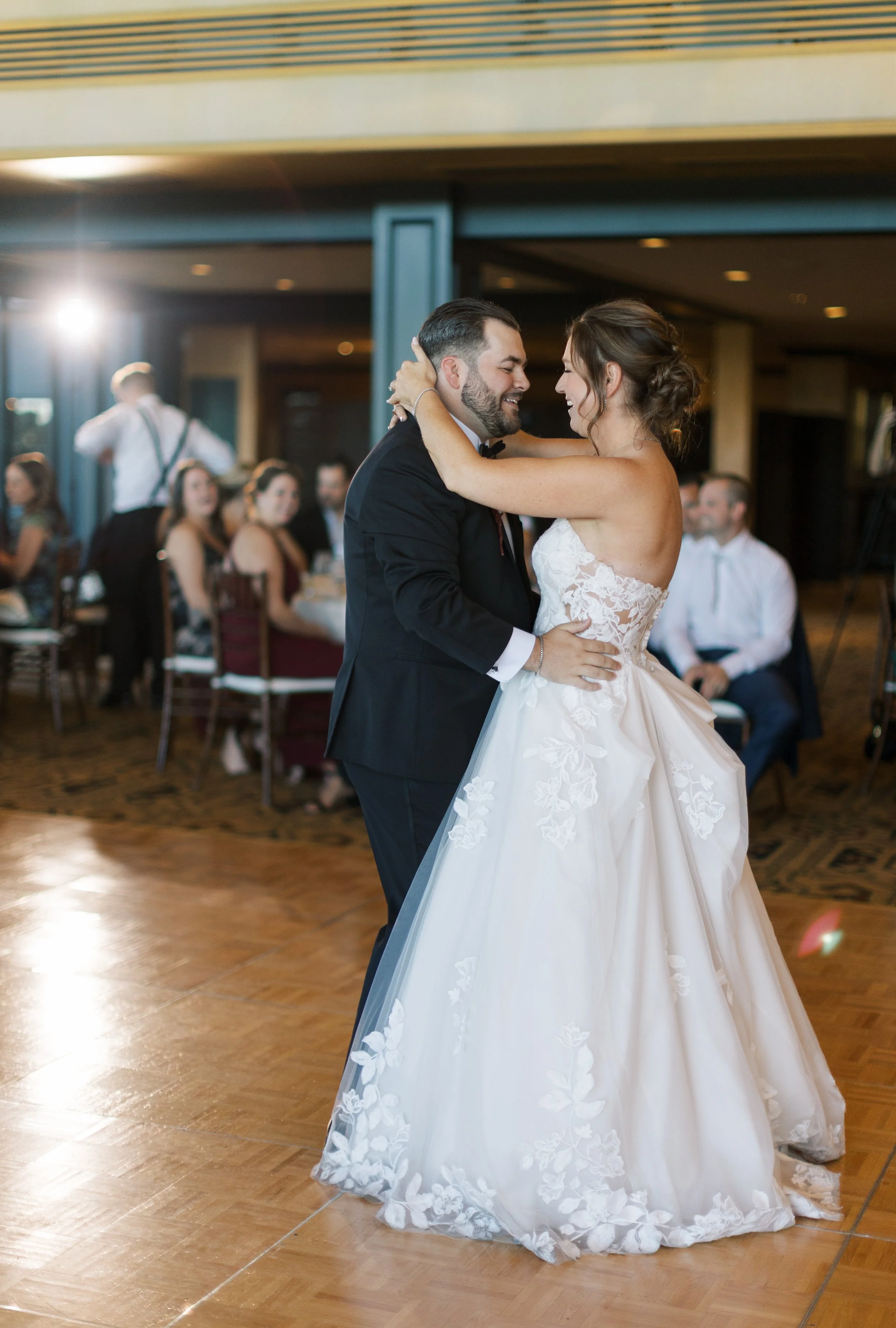 A bride and groom dancing closely at their wedding reception, with guests watching in the background.