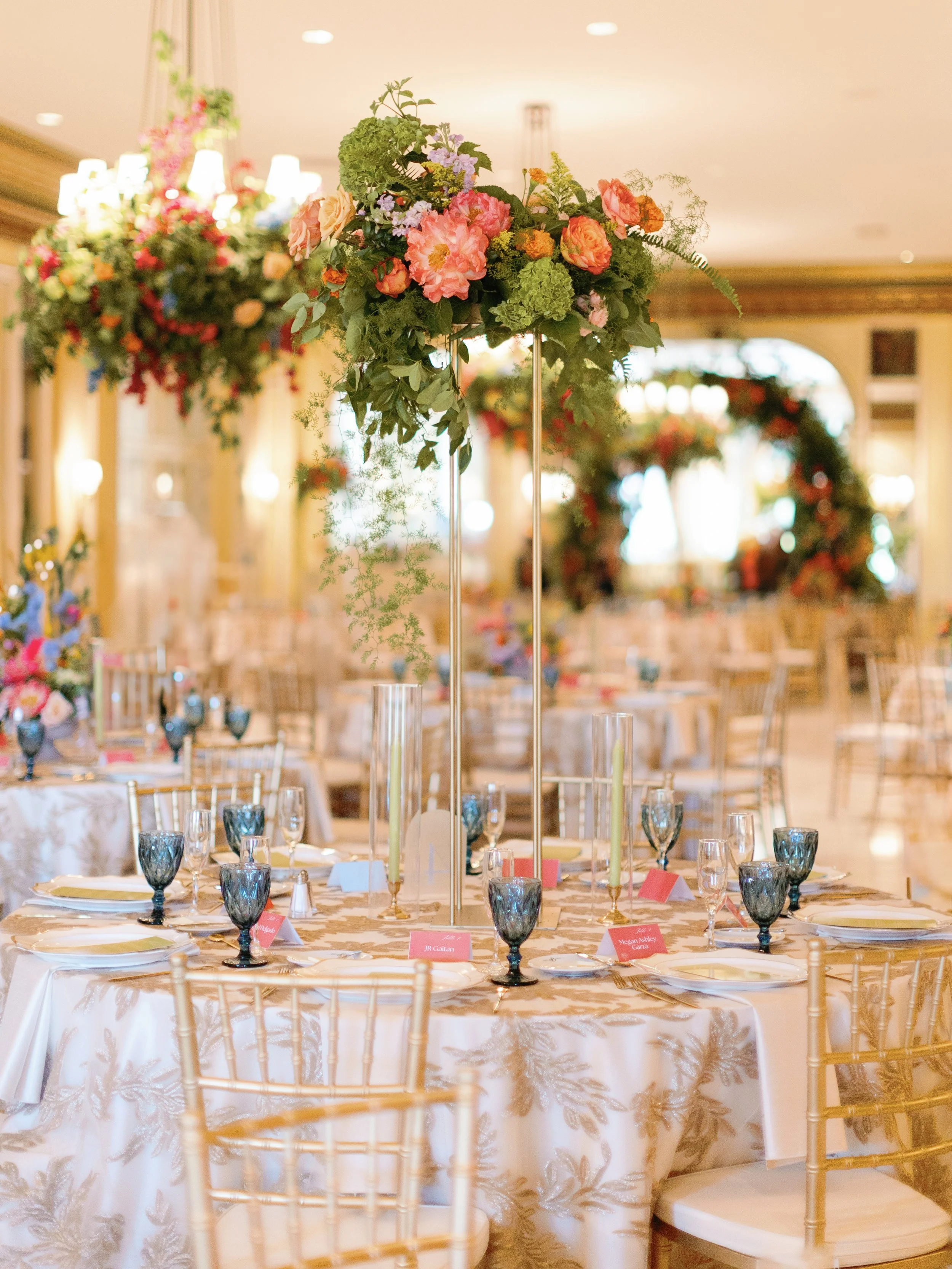 Elegant banquet table setup with floral centerpieces, gold chairs, and decorative tableware in an ornate event hall.