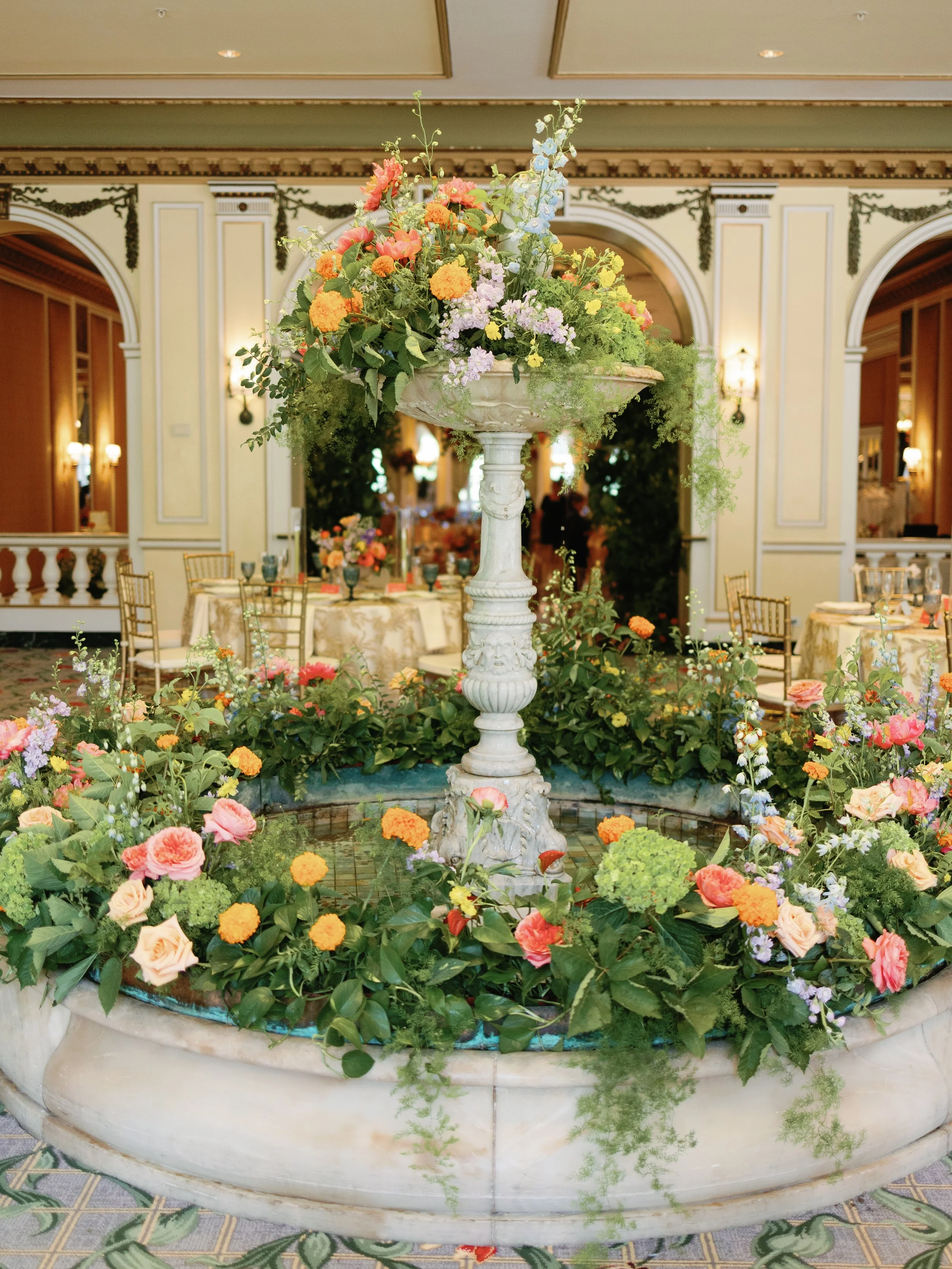Decorative indoor fountain surrounded by colorful flowers in an elegant banquet hall.