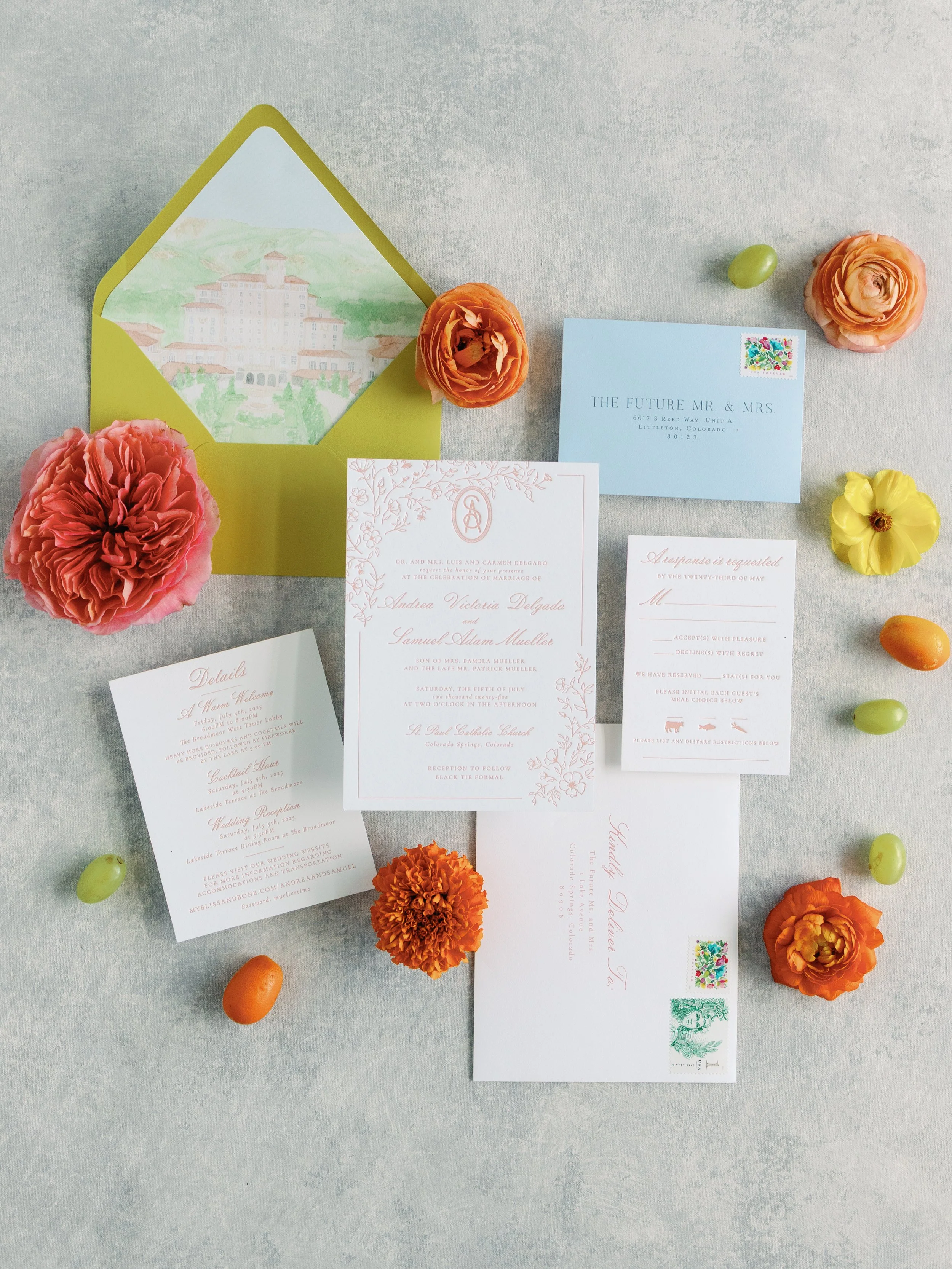 Wedding invitation suite with floral accents, including an envelope, RSVP card, dress code card, and invitation card, surrounded by colorful flowers and candies on a light surface.