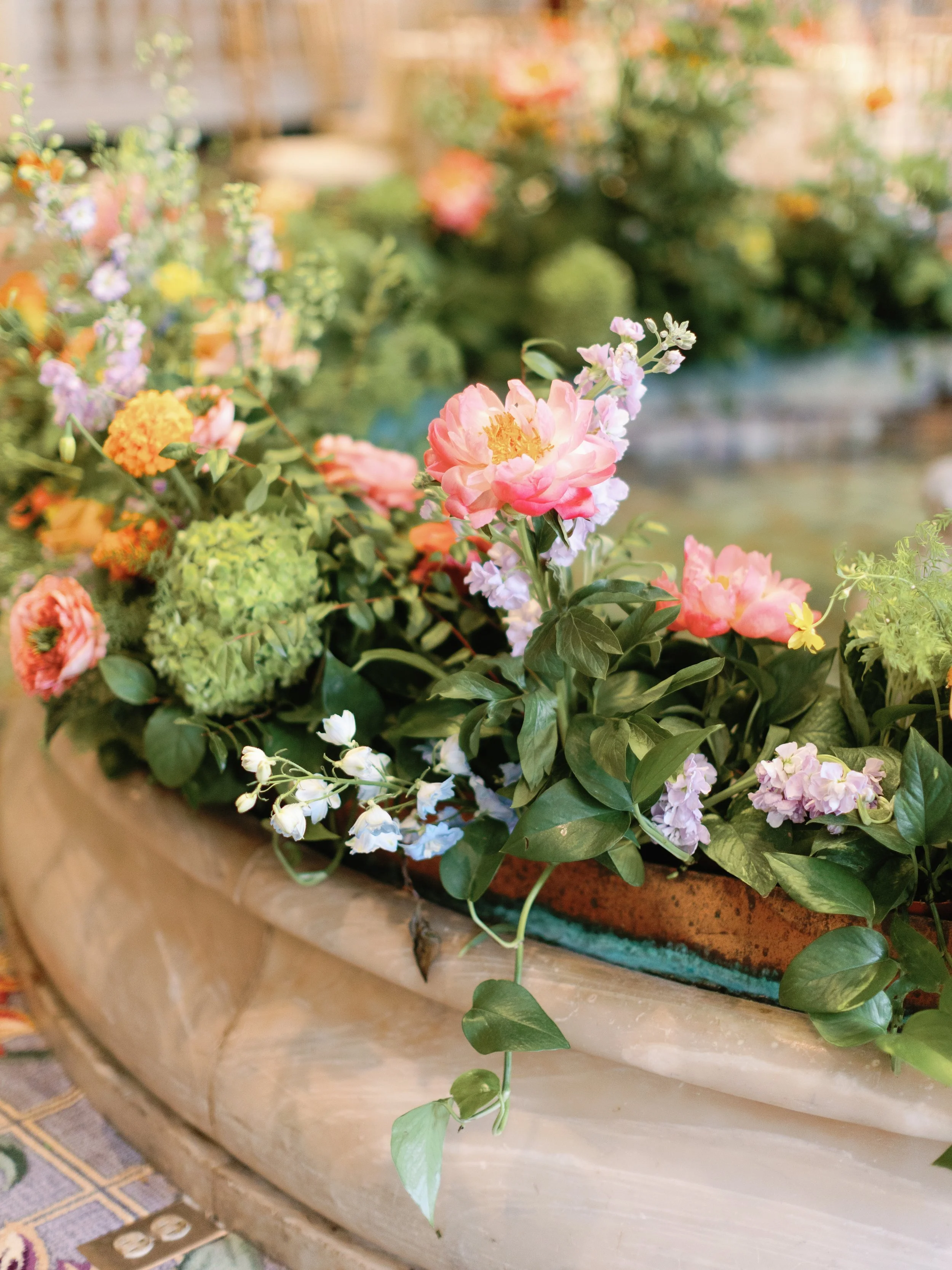 Colorful flower arrangement with pink, orange, purple, and white blossoms in a stone or ceramic container.