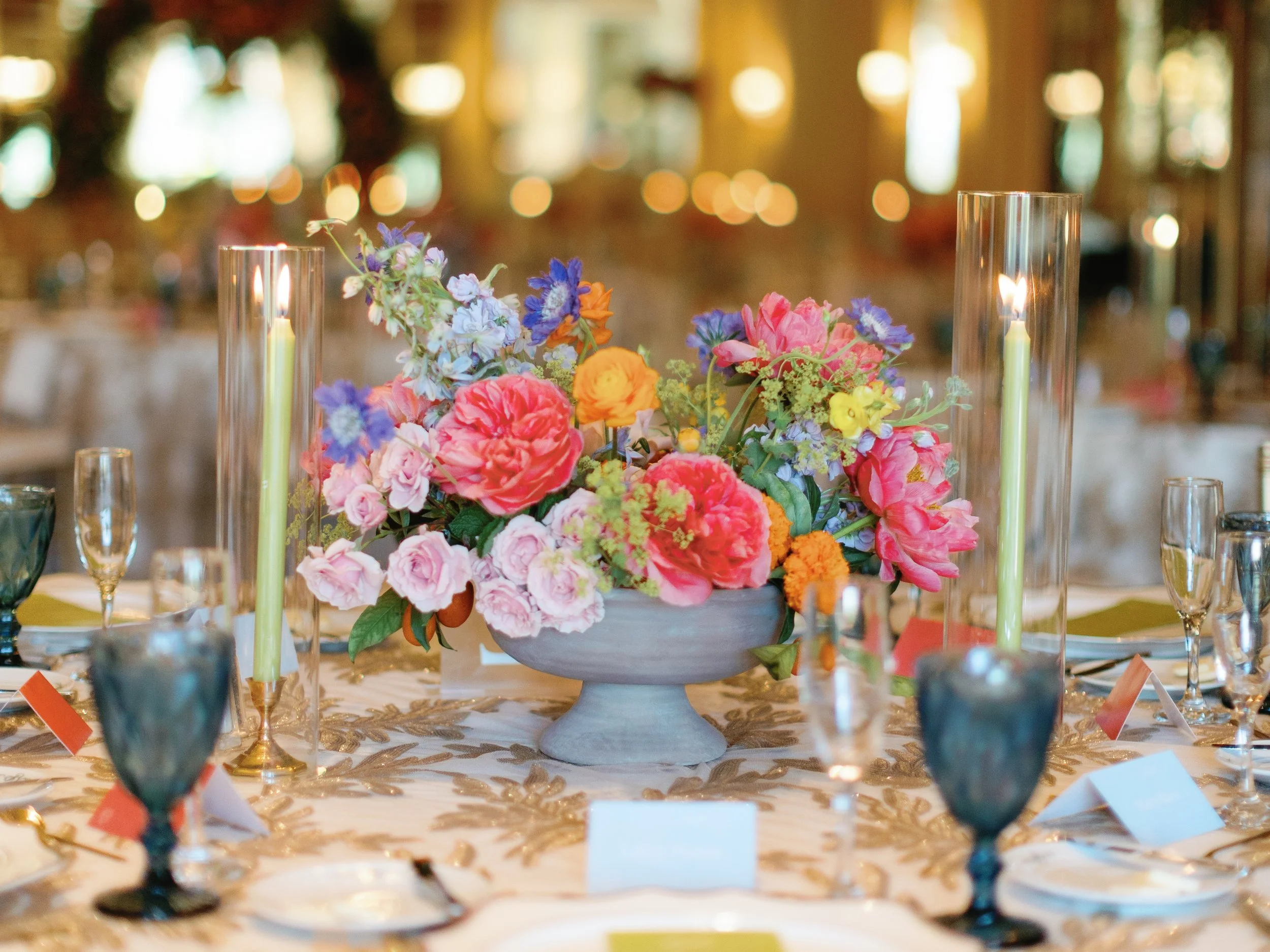 A centerpiece with pink, purple, orange, and yellow flowers on a decorated dinner table at an event.