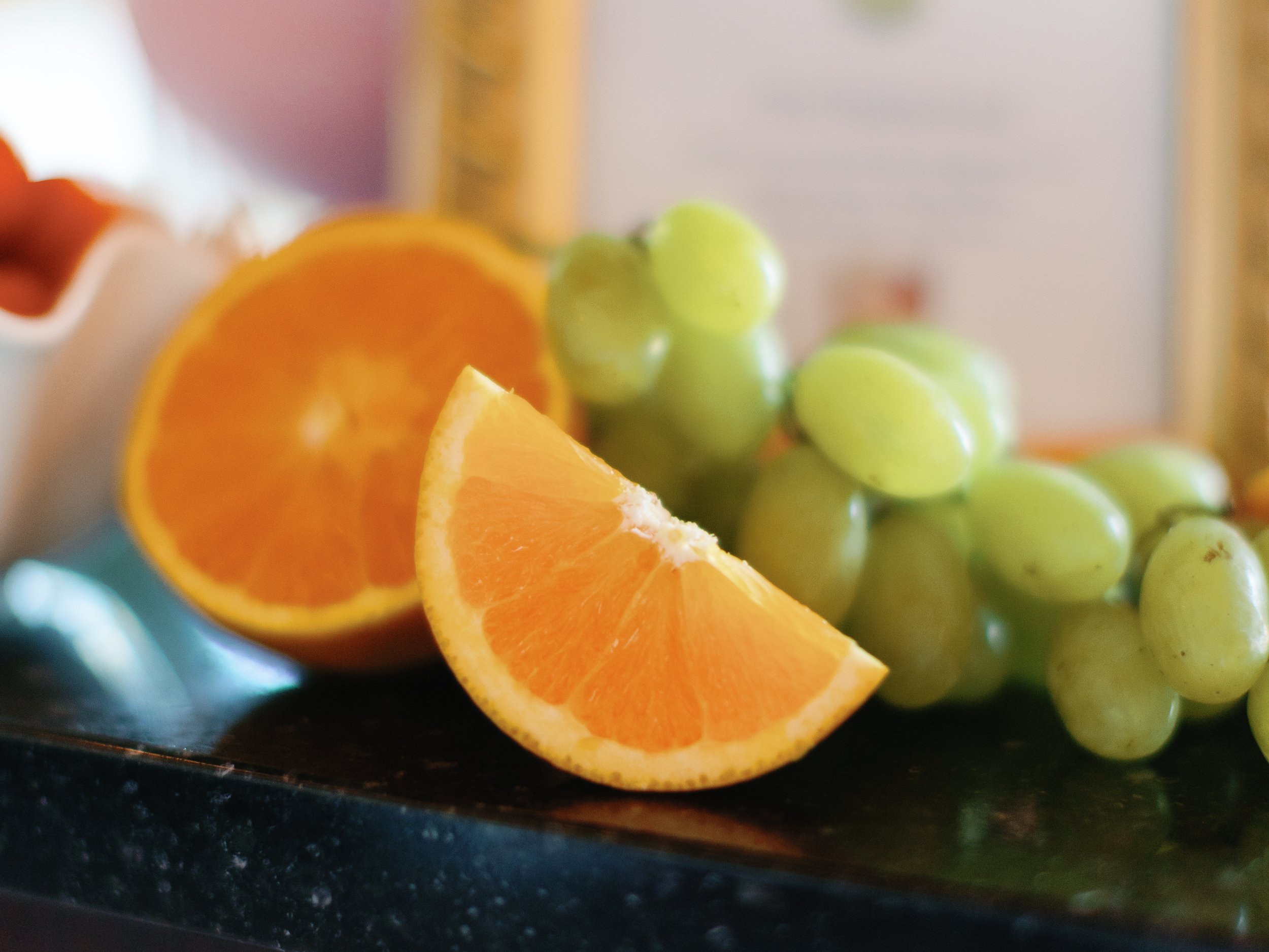 Close-up of orange and green grapes on a black surface with a blurred background.
