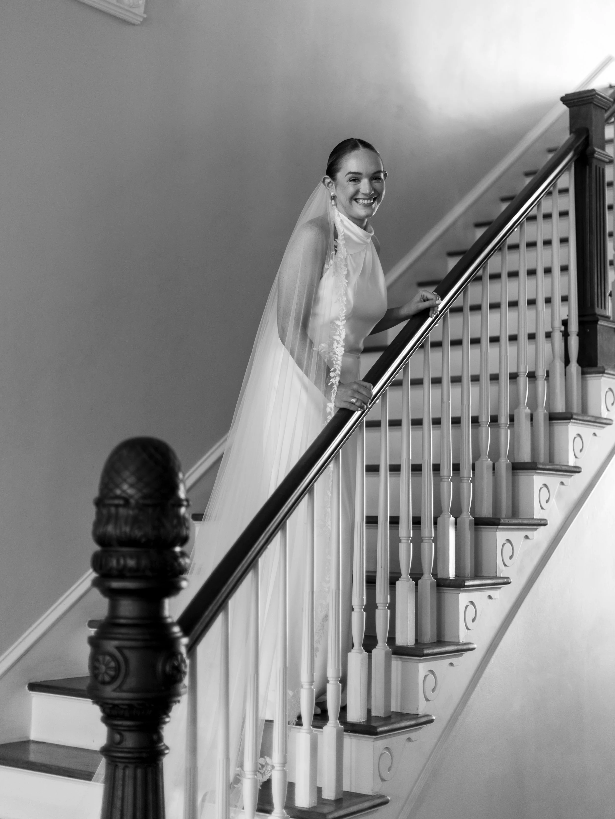 A bride in a wedding dress and veil smiling on a staircase.