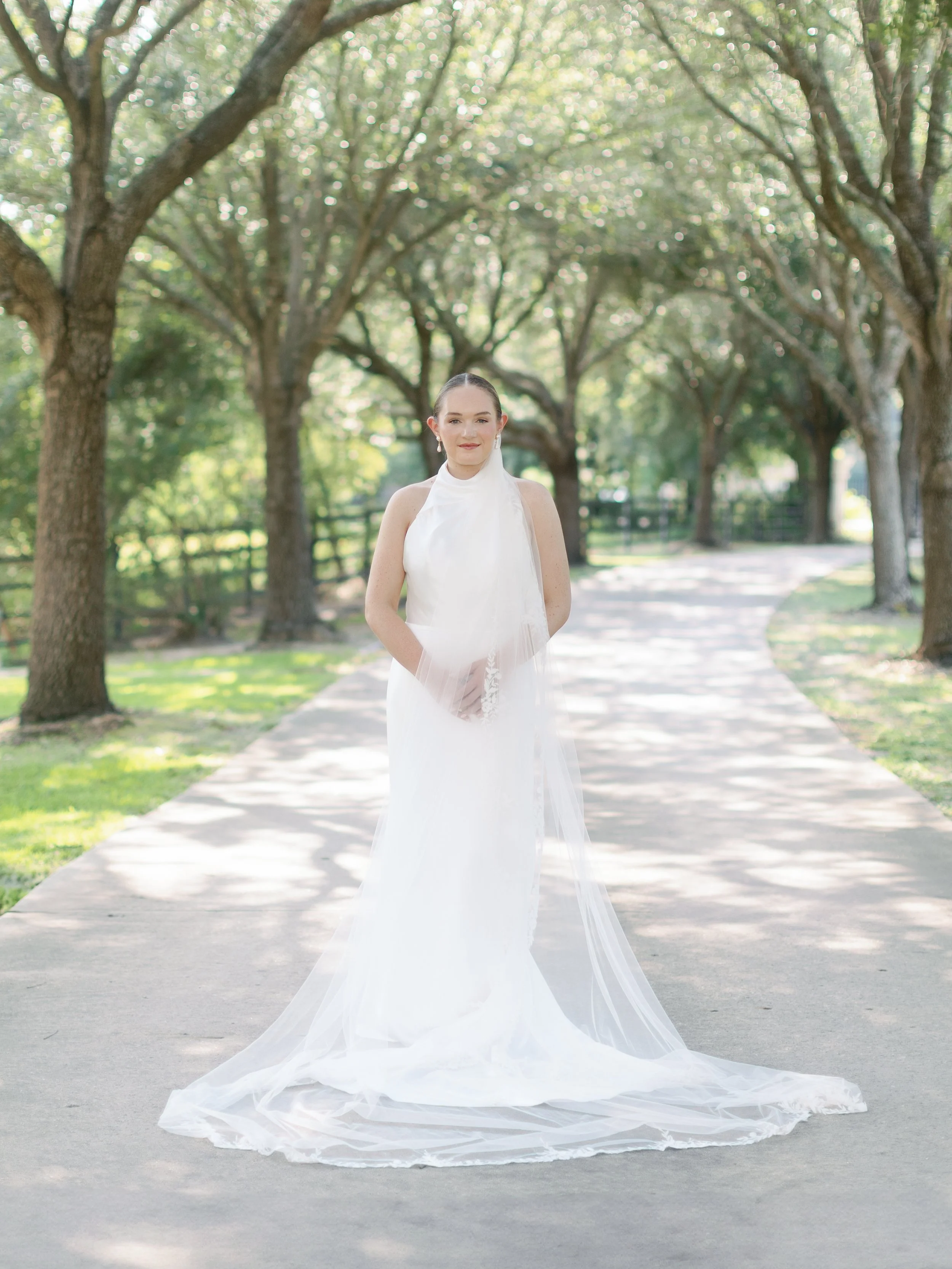A woman in a white wedding dress standing on a tree-lined pathway.