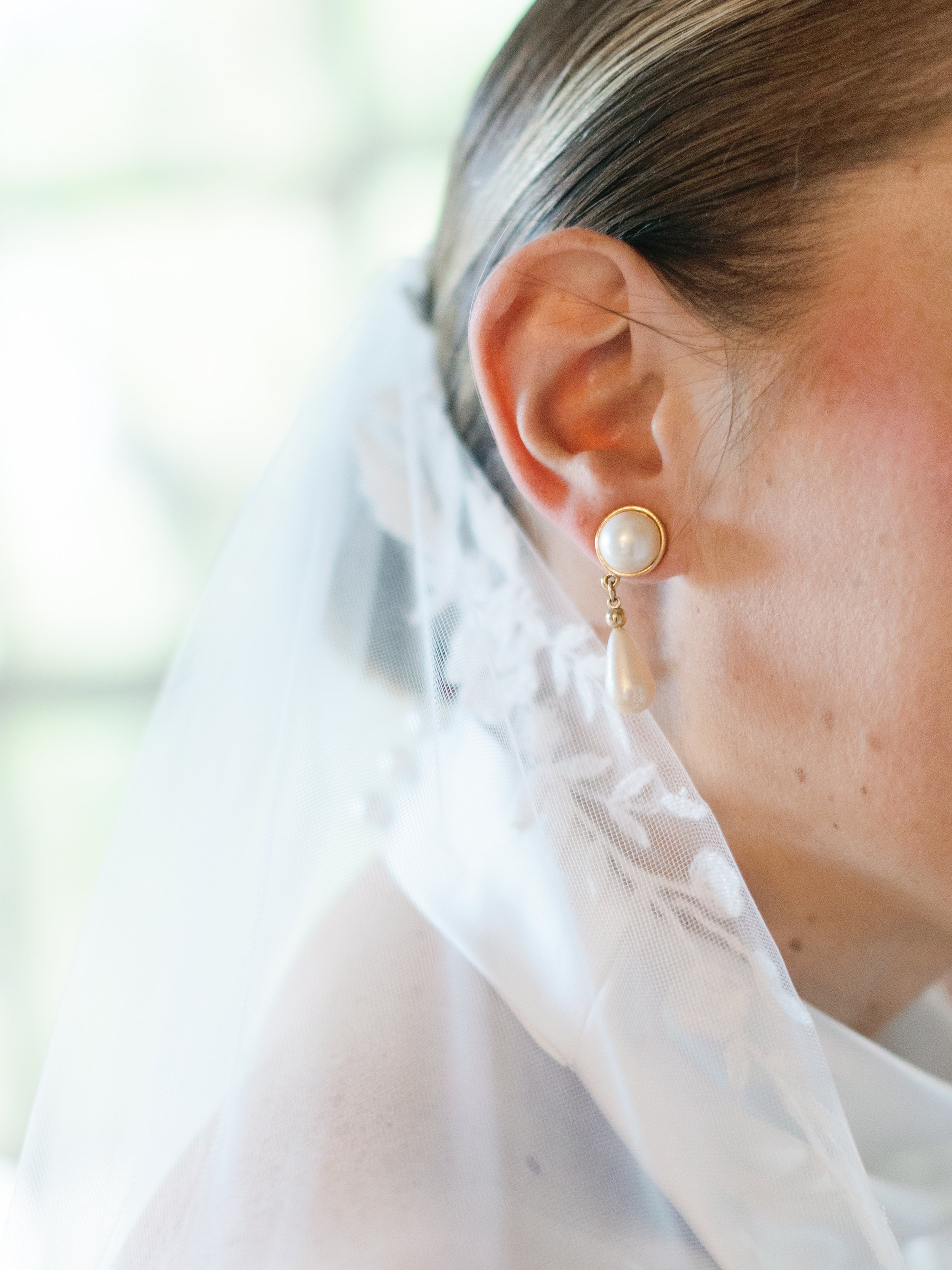 Close-up of a woman's ear with a pearl earring and wedding veil.