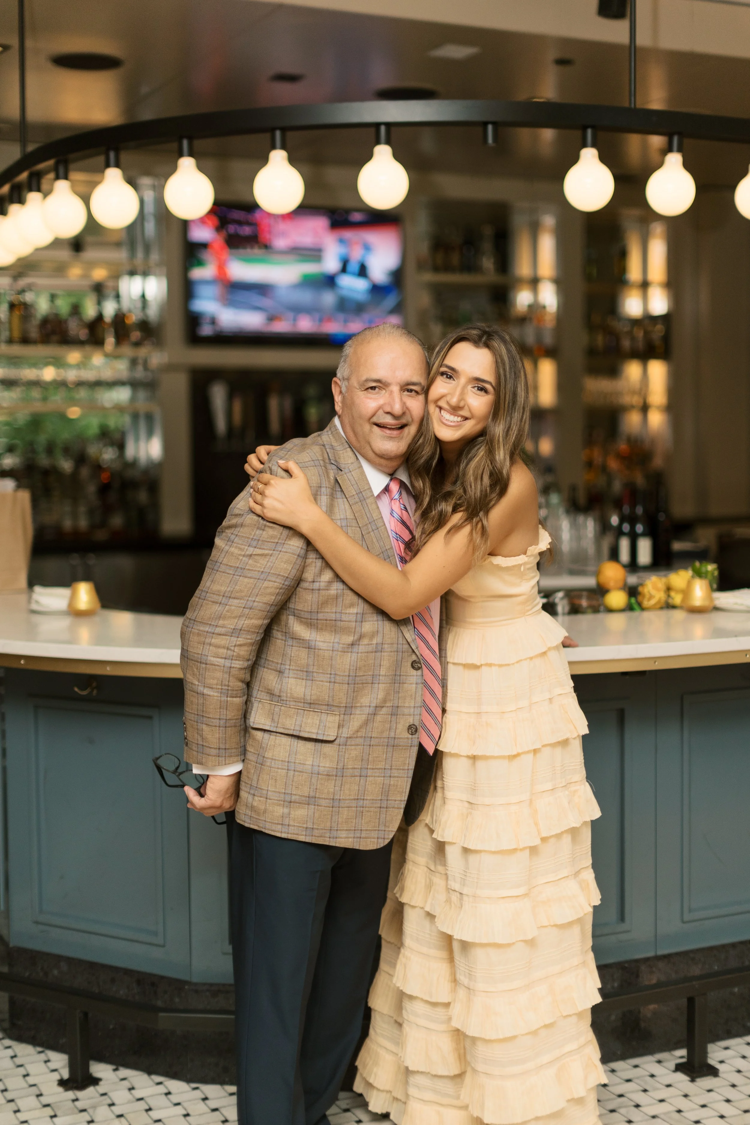 A man and a woman hugging in a restaurant or bar setting, smiling at the camera.
