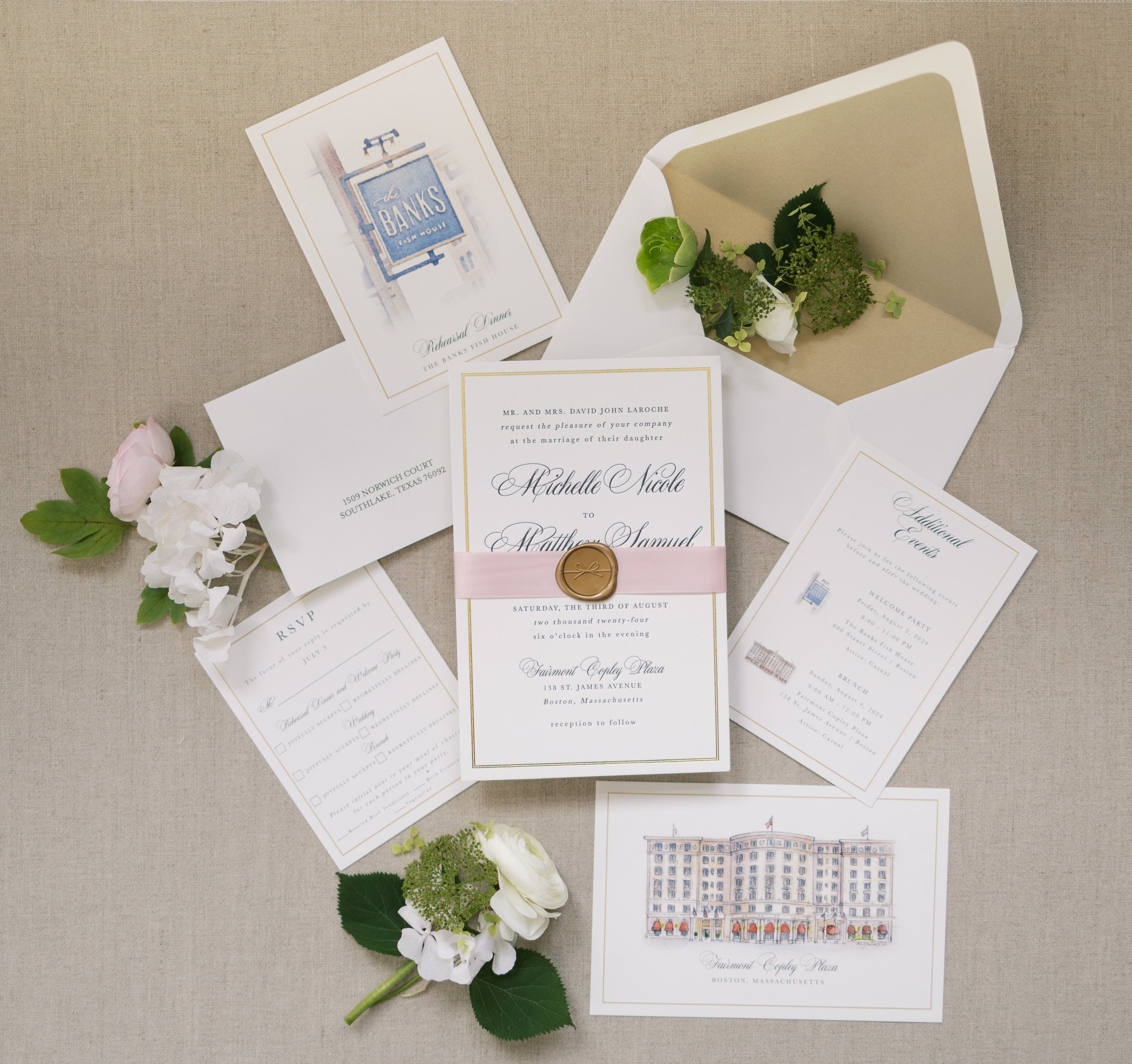 Wedding invitation suite with floral accents, including an envelope, RSVP card, additional event details, and a small drawing of a building, arranged on a beige surface.