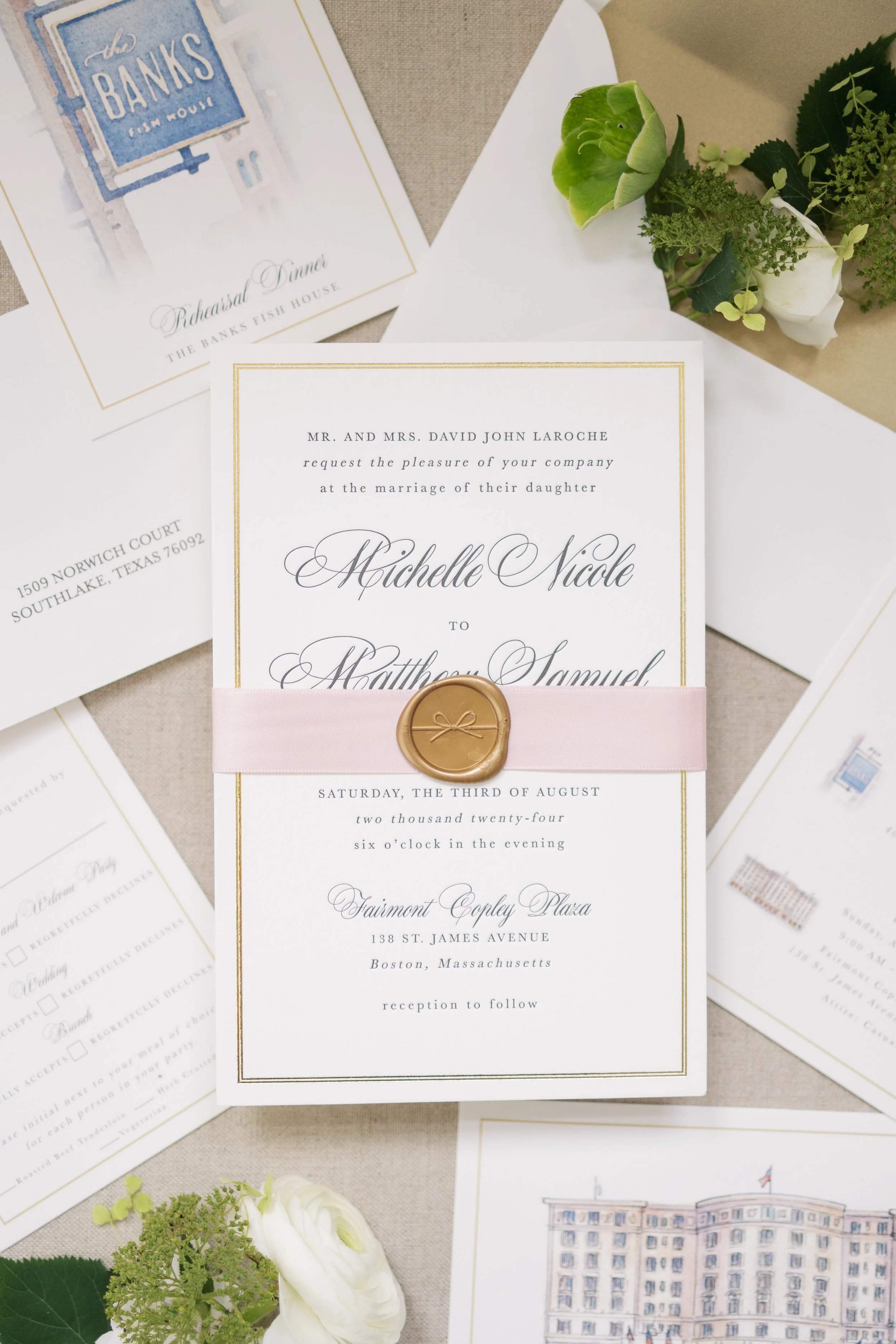 Wedding invitation with a pink ribbon and gold wax seal, surrounded by other wedding stationery and floral arrangements.