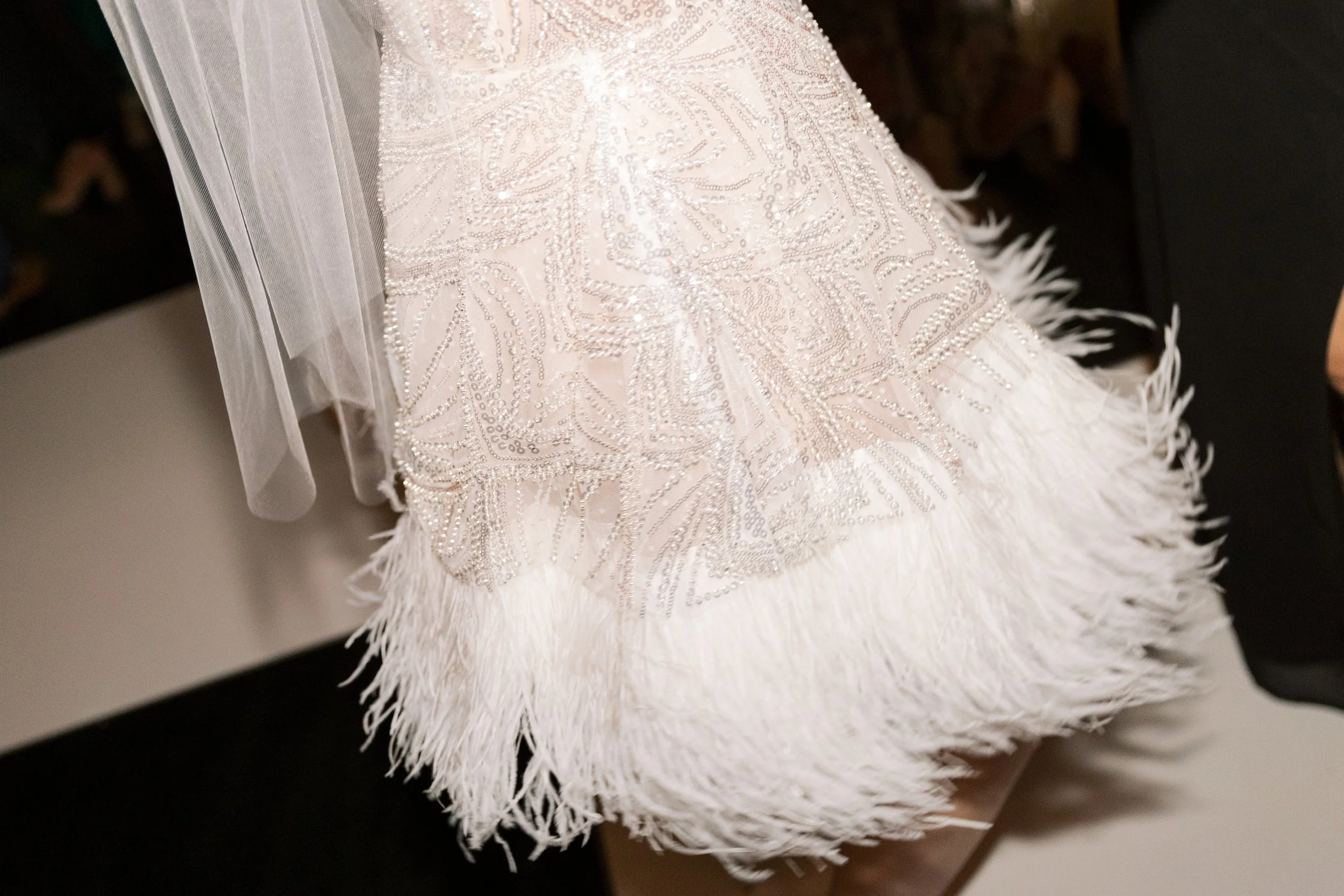 Close-up of a white dress with beadwork and feather details.