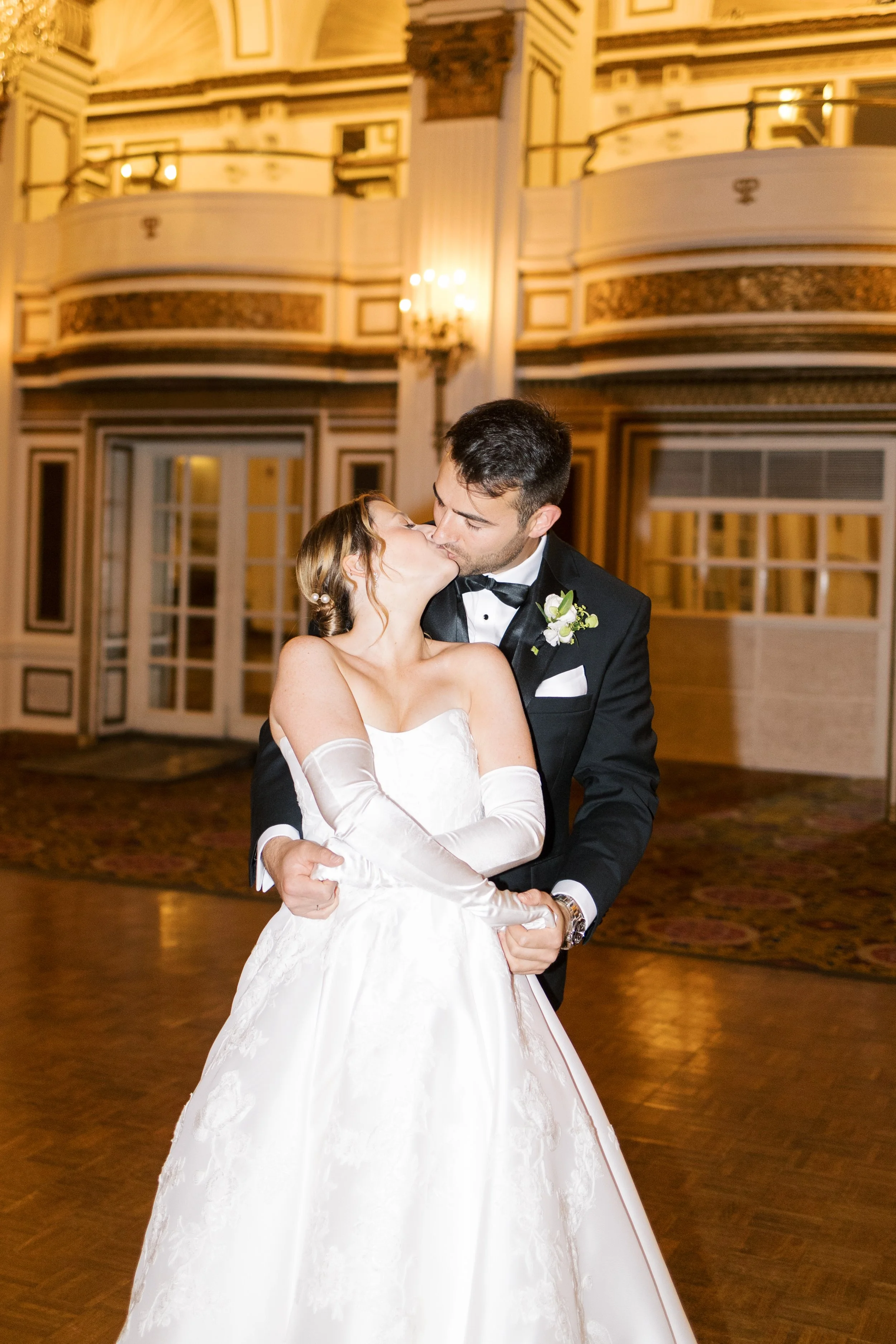 A bride and groom sharing a kiss at their wedding reception in an elegant ballroom.