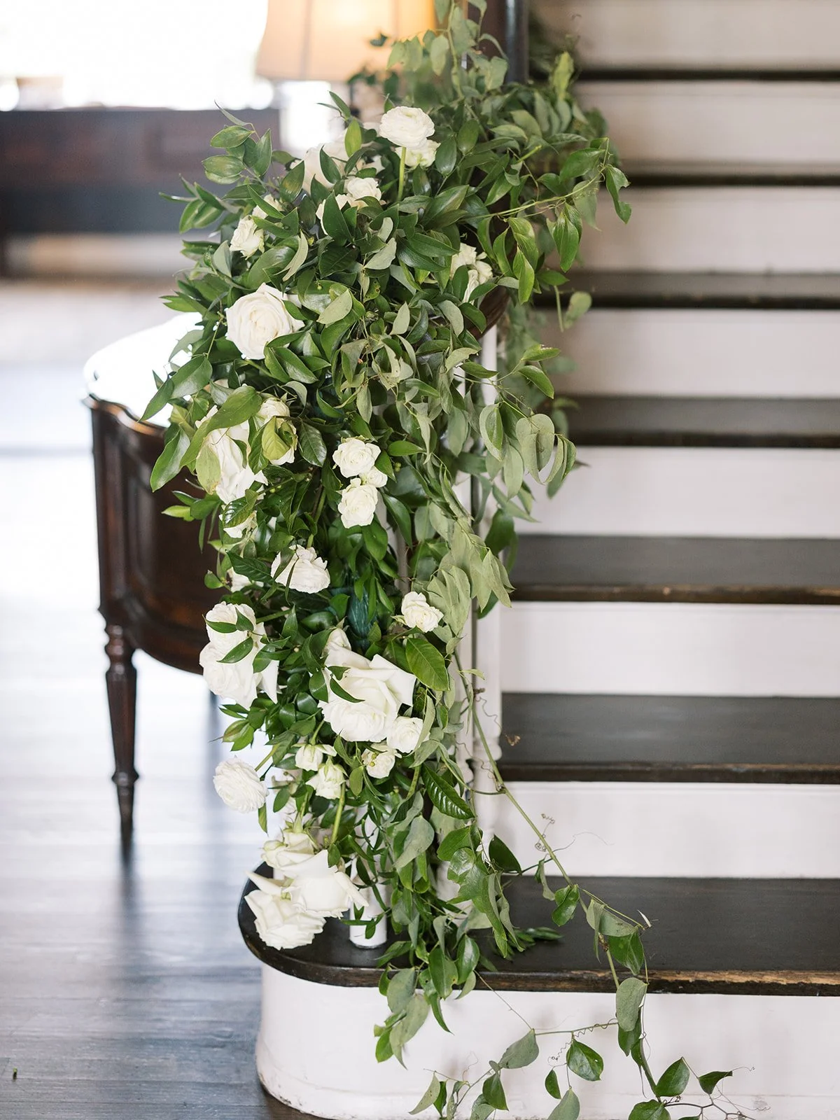 Green leafy garland with white flowers draped along a staircase railing.