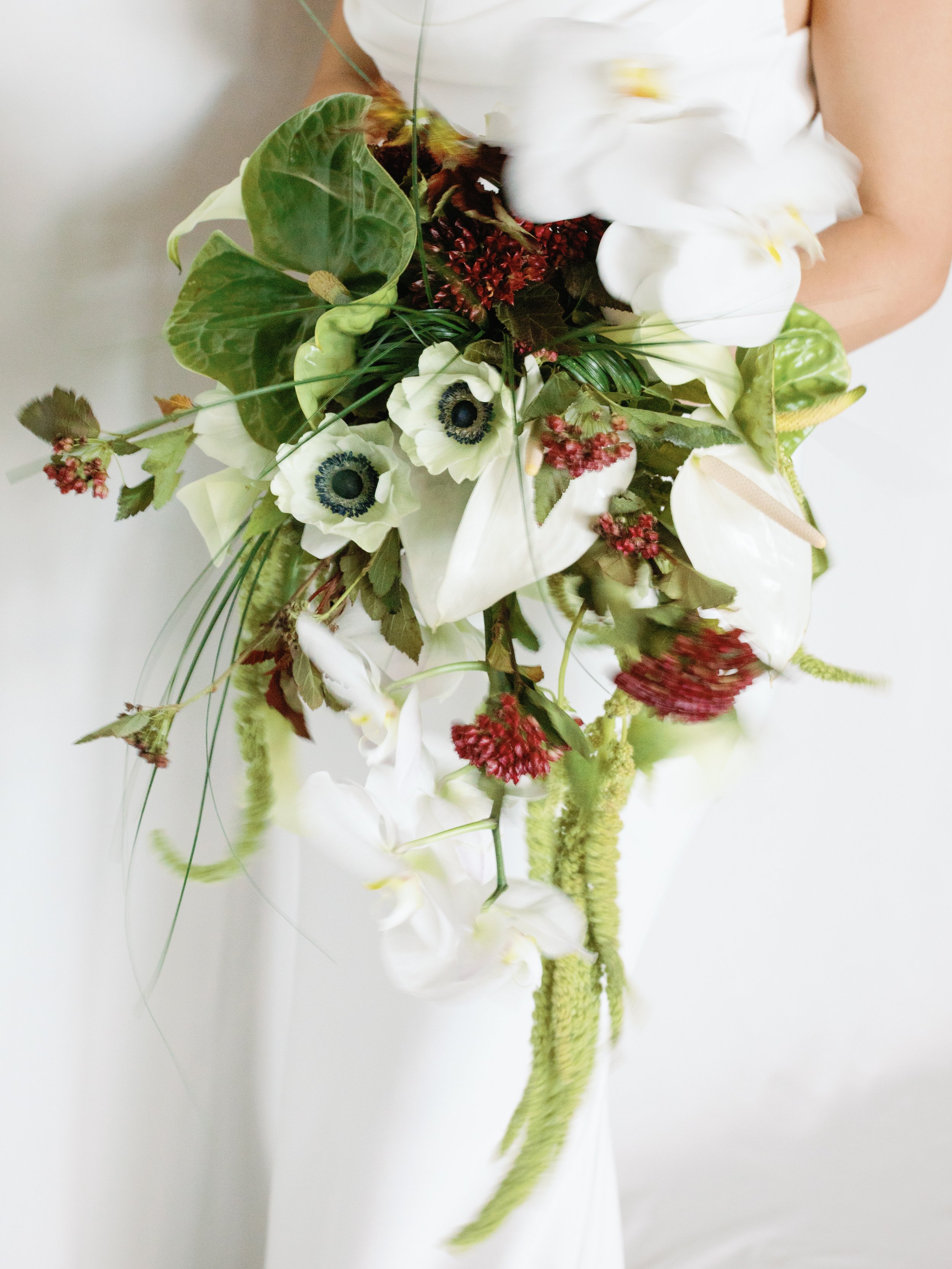 A person in a white dress holding a bouquet of various flowers and greenery.