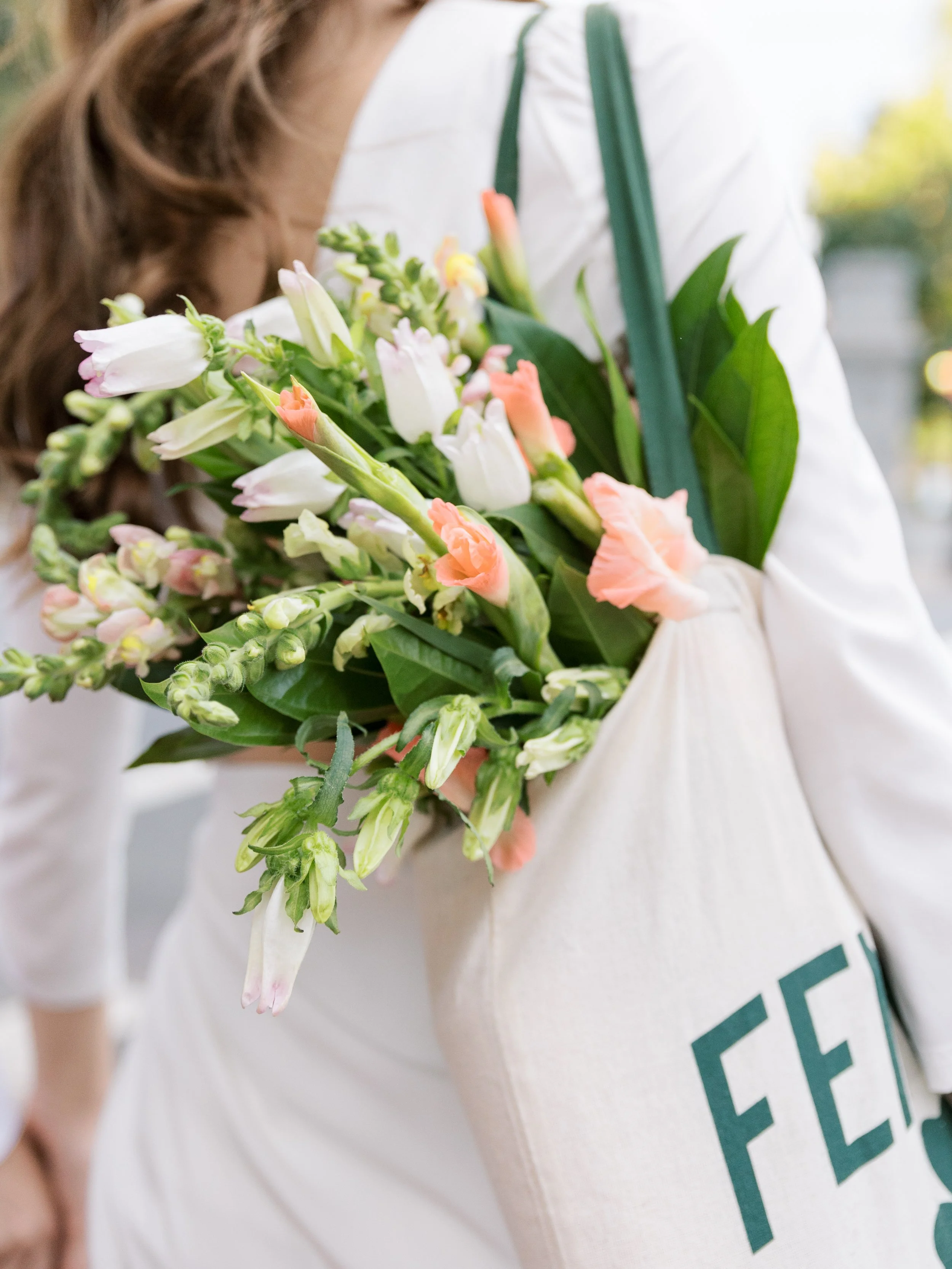 Person holding a bouquet of pink and white flowers with green leaves, wearing a white shirt and green straps.