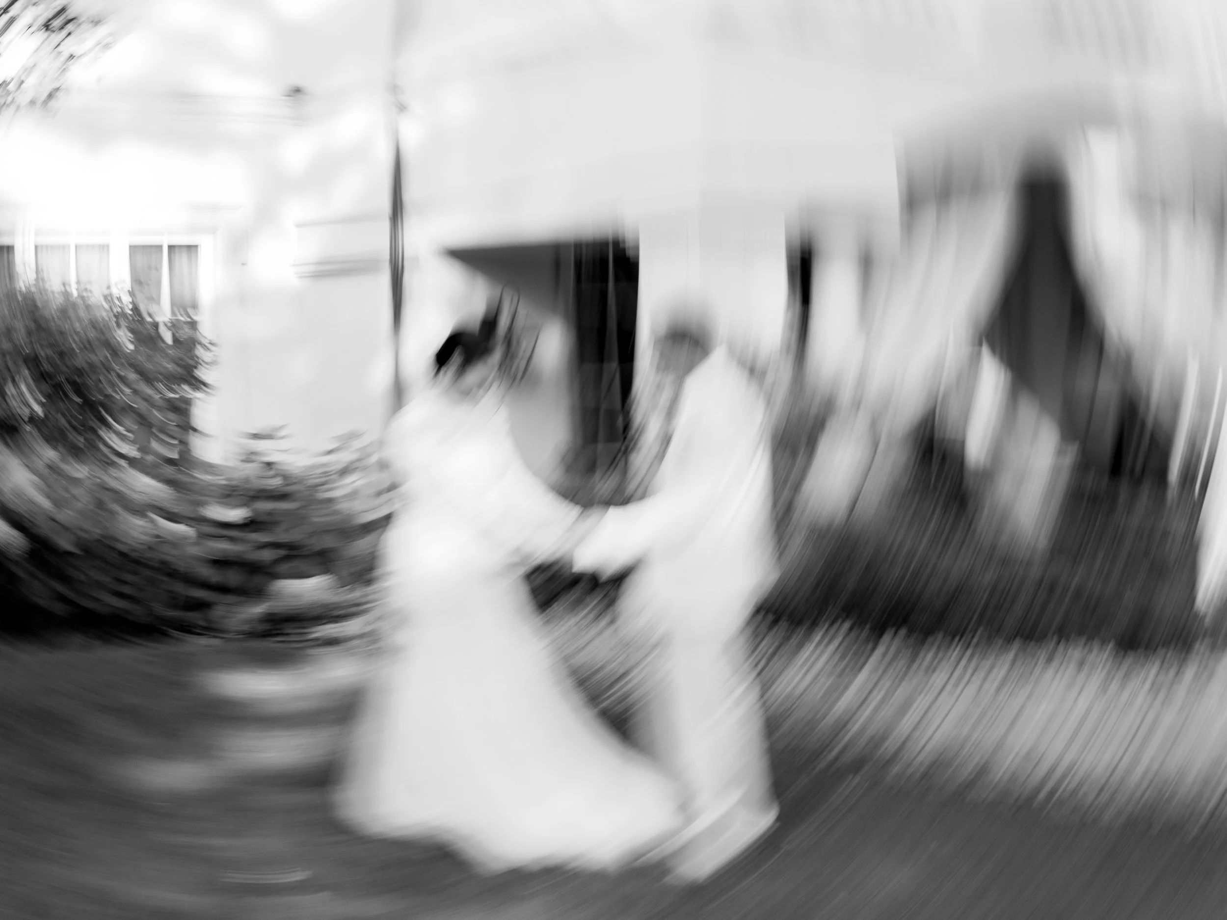 Black and white photo of a couple dancing outside a house, with a blur effect.