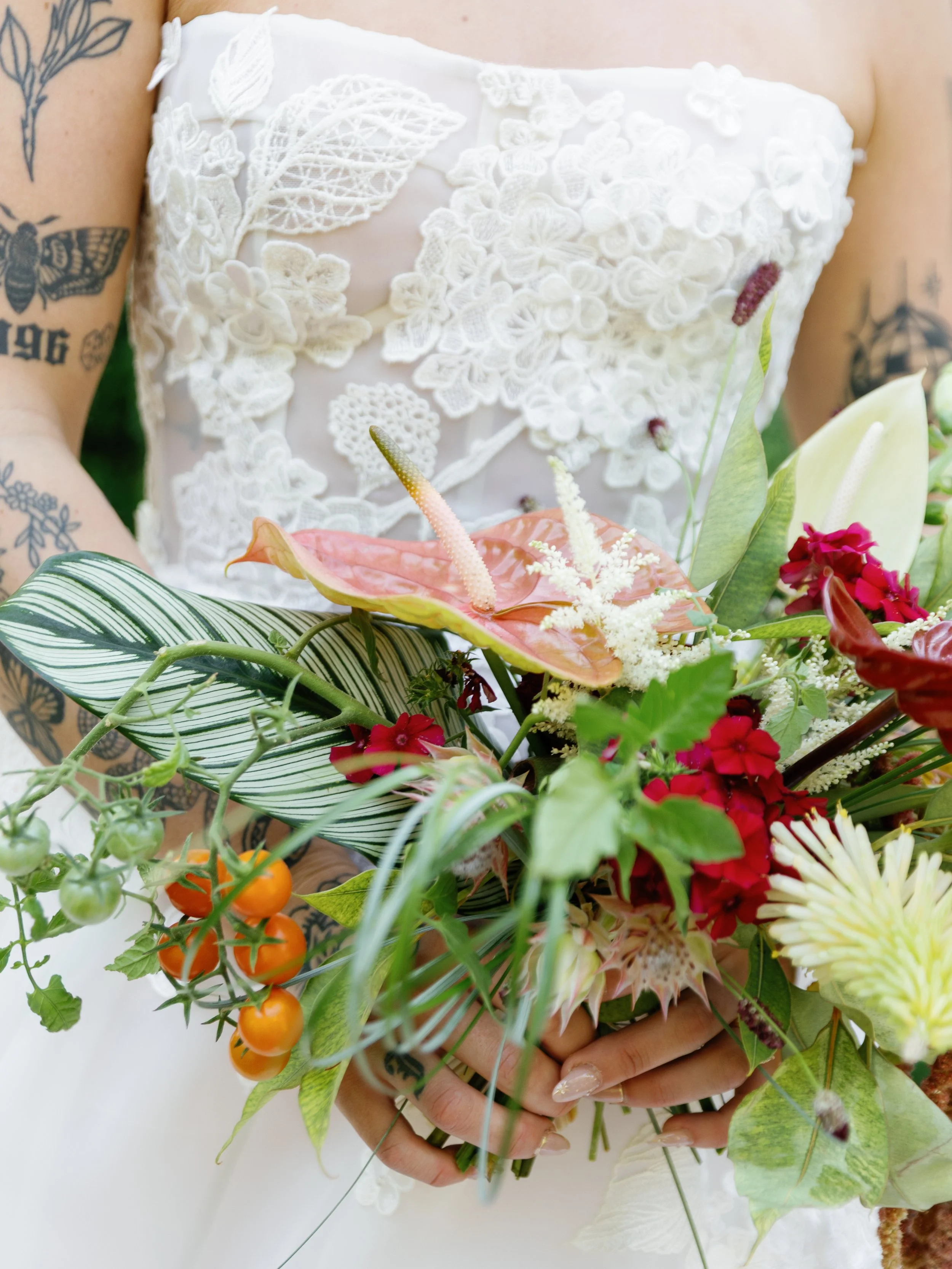 Bride holding a colorful bouquet of flowers in front of her white lace wedding dress