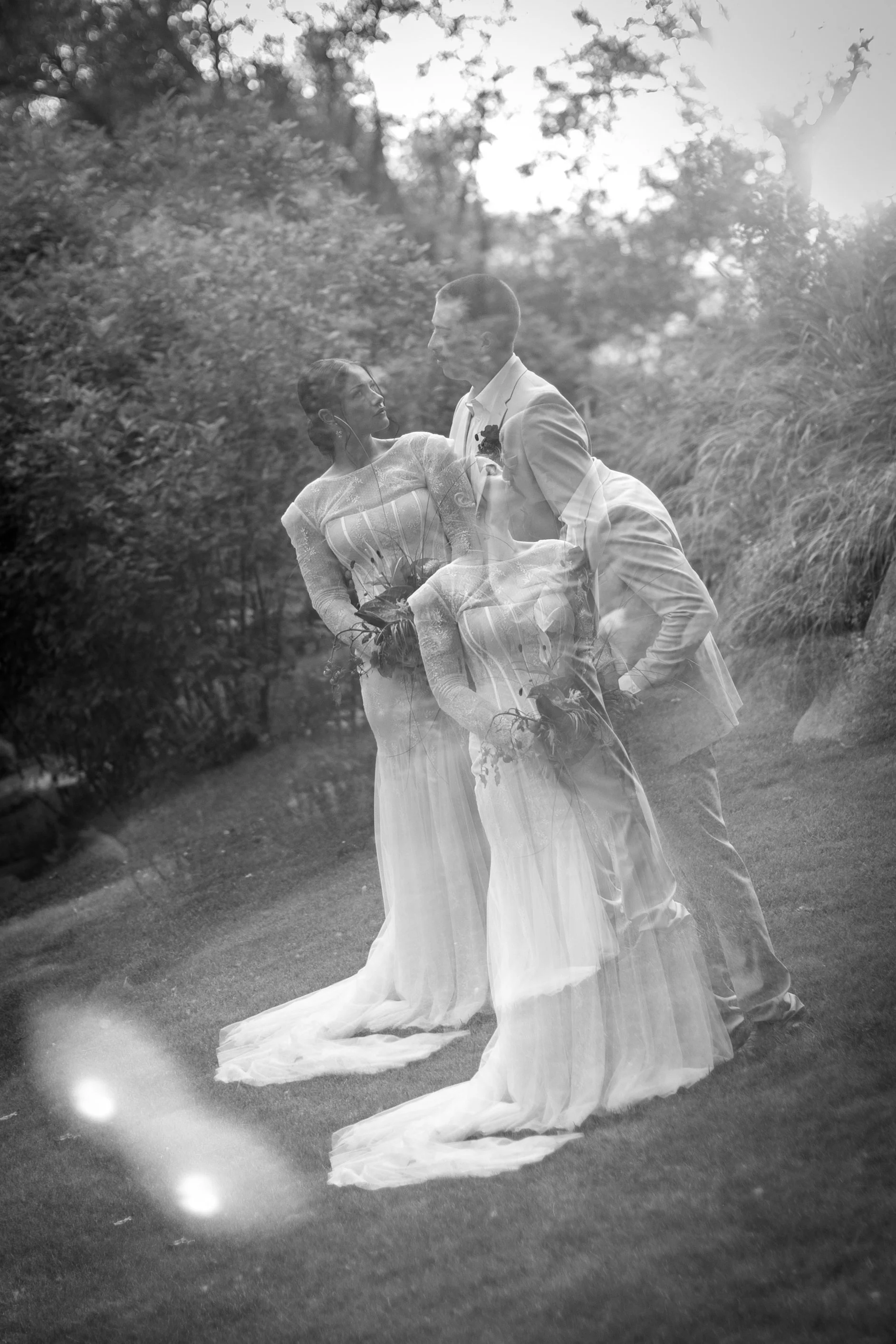 Black and white photo of a wedding couple outdoors, with the photo taken through a window creating a layered effect.