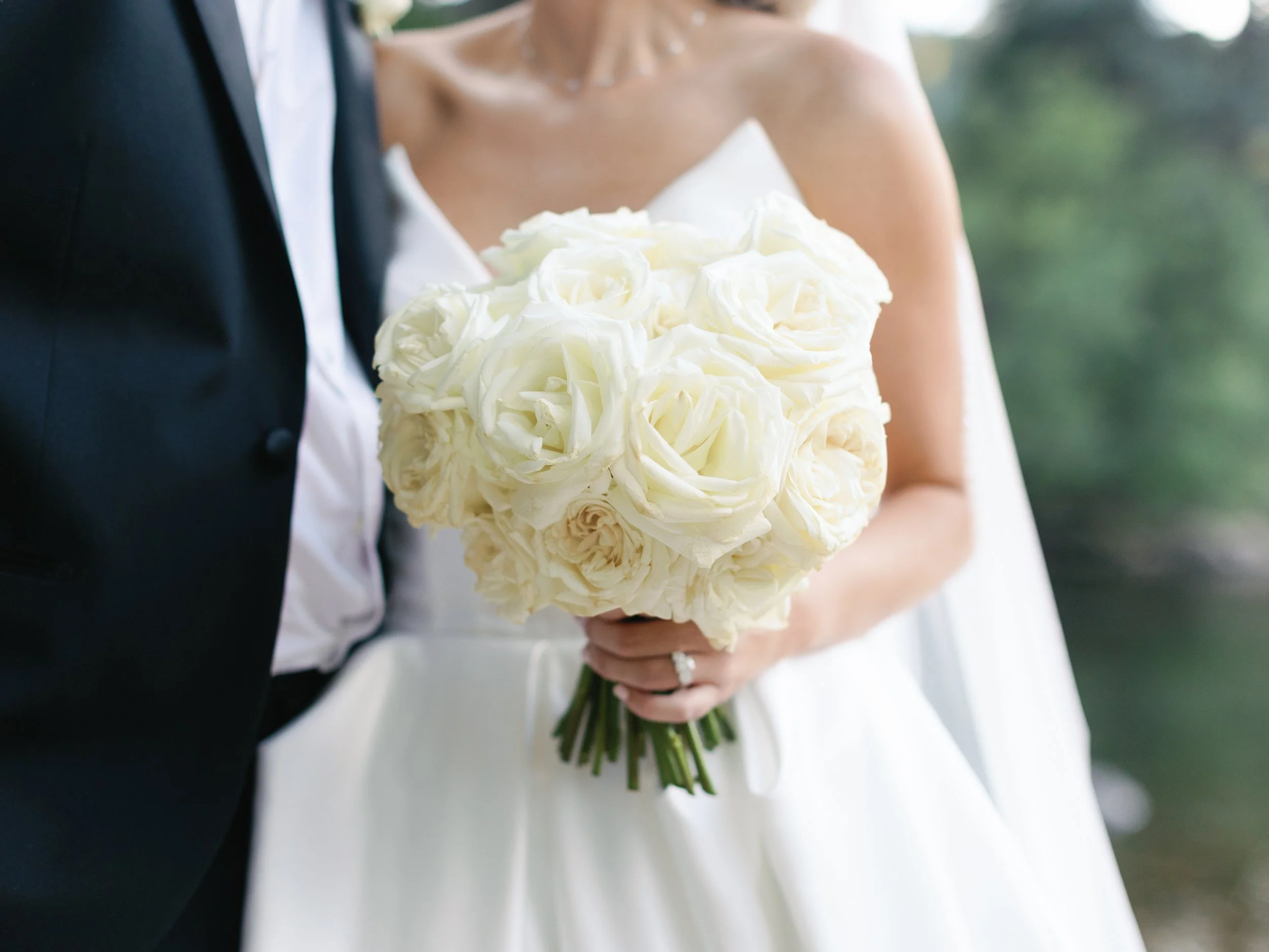 Bride holding a bouquet of white roses, standing next to her groom in a wedding photo.