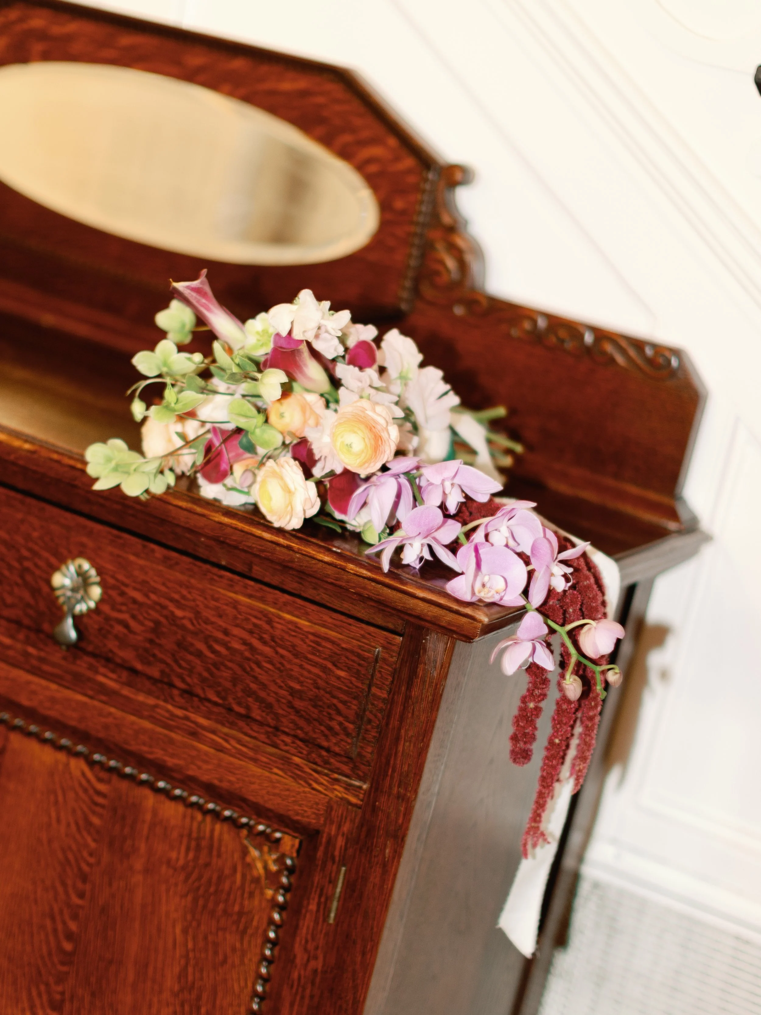 A bouquet of colorful flowers resting on a vintage wooden dresser with a mirror.