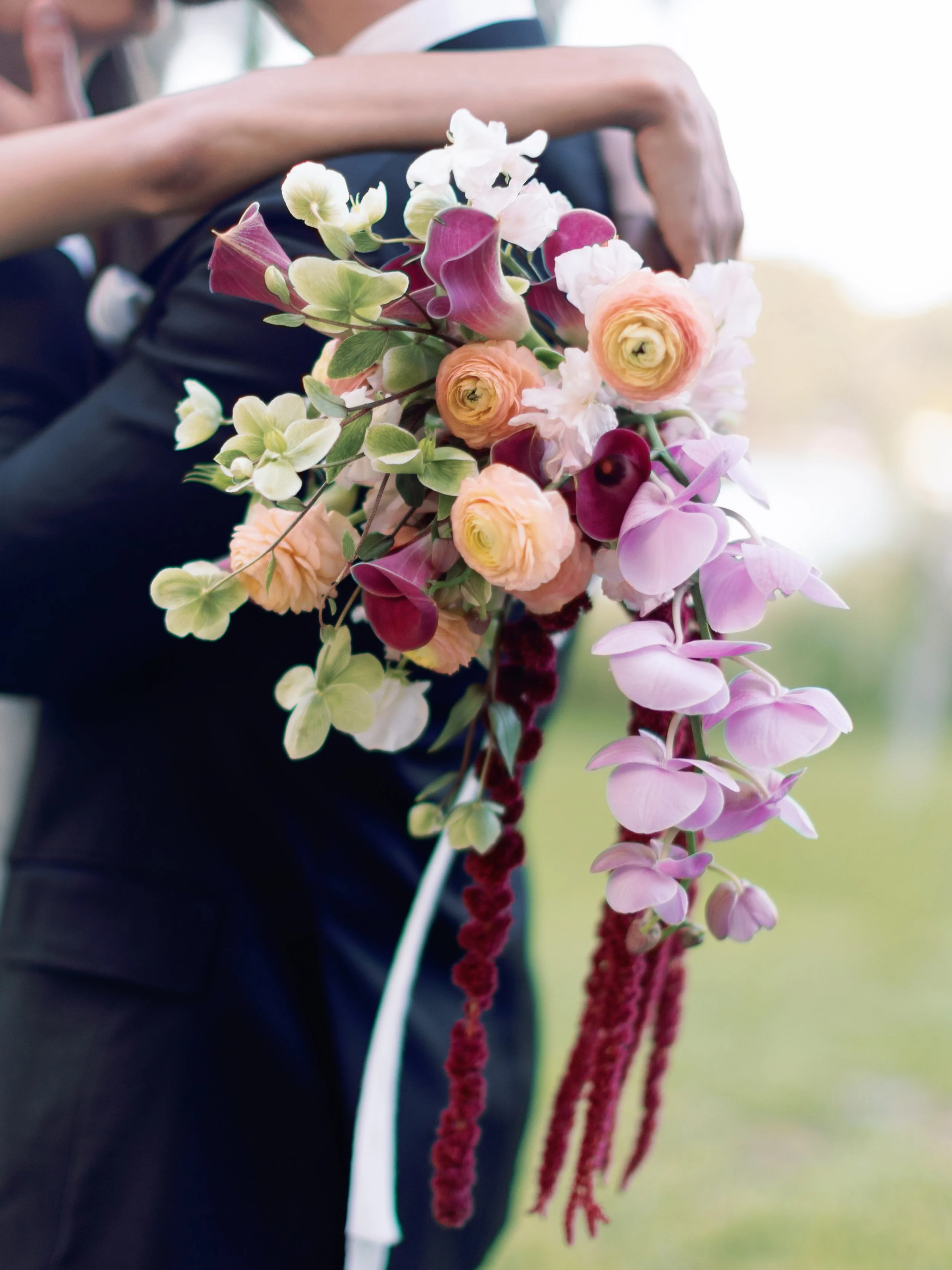 A wedding couple holding a large bouquet of pink, white, and purple flowers.