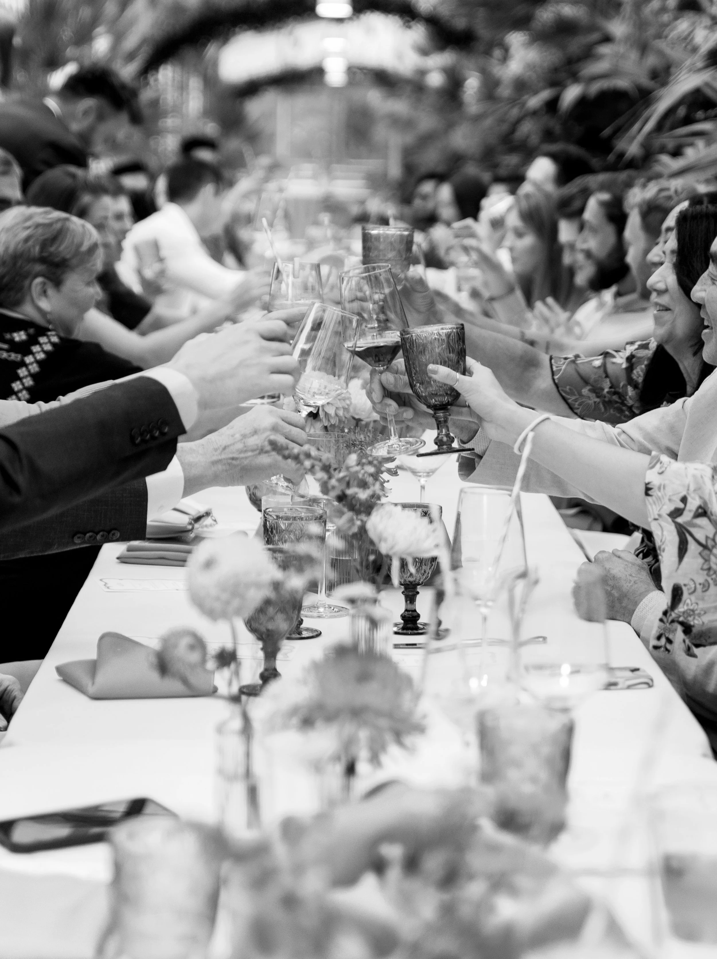 People at a long table celebrating with wine and drinks in an outdoor setting, raising glasses in a toast.