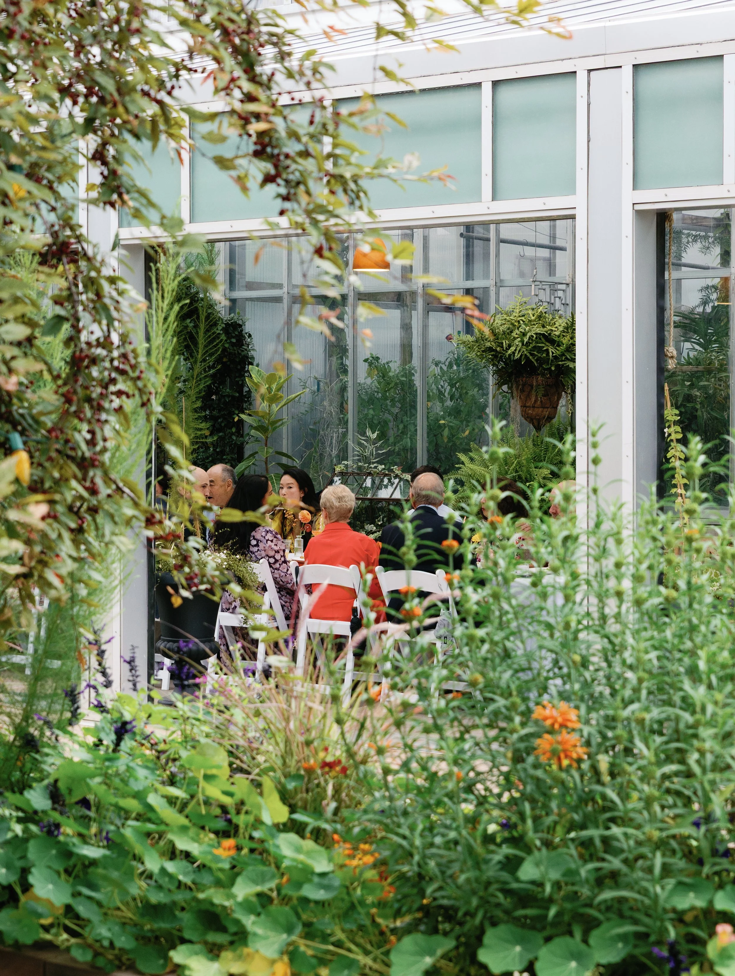 People sitting at a table inside a greenhouse surrounded by lush green plants and flowers.