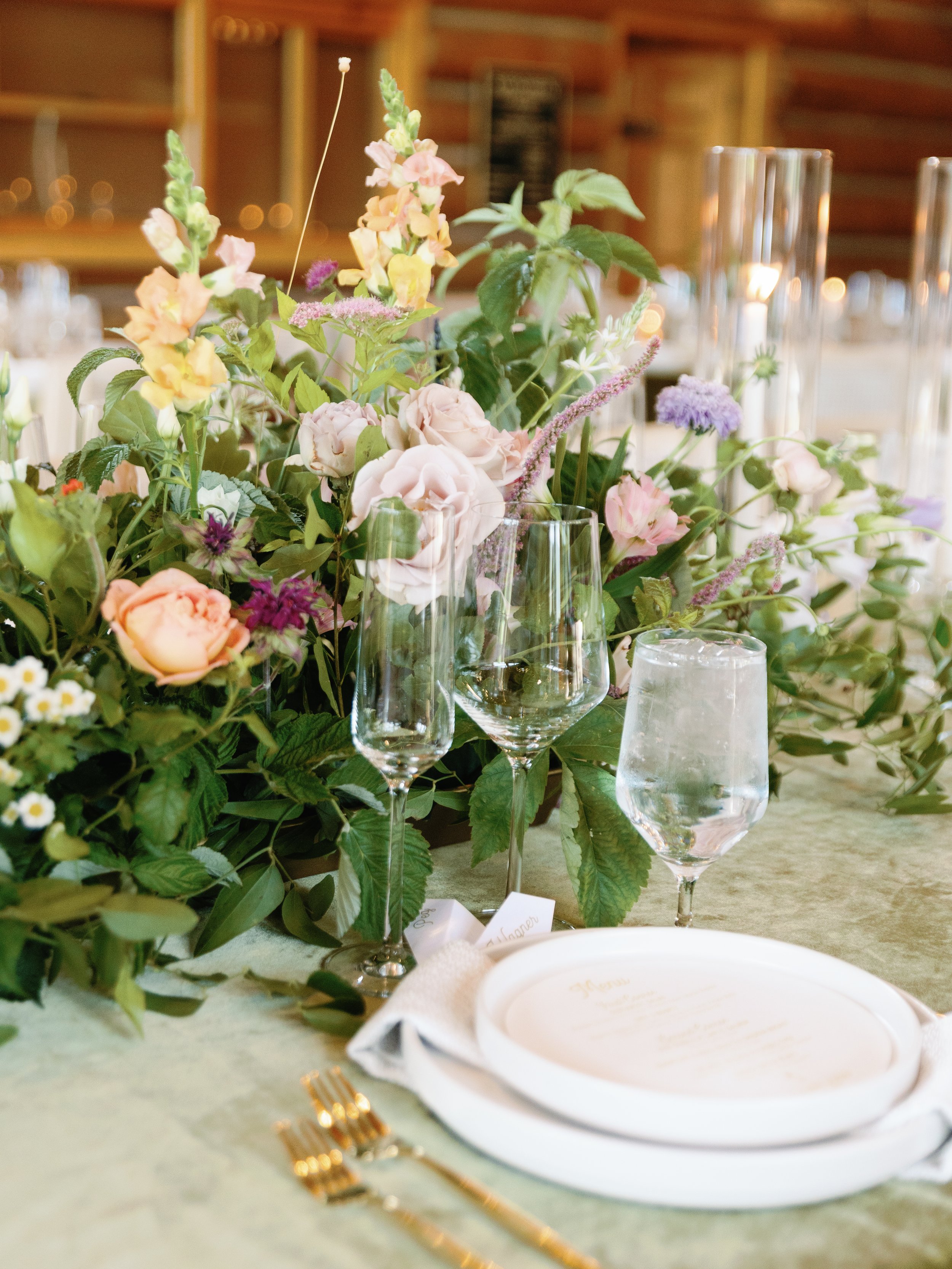 A wedding or elegant event table setting with glassware, a floral centerpiece, and a plate with gold cutlery.
