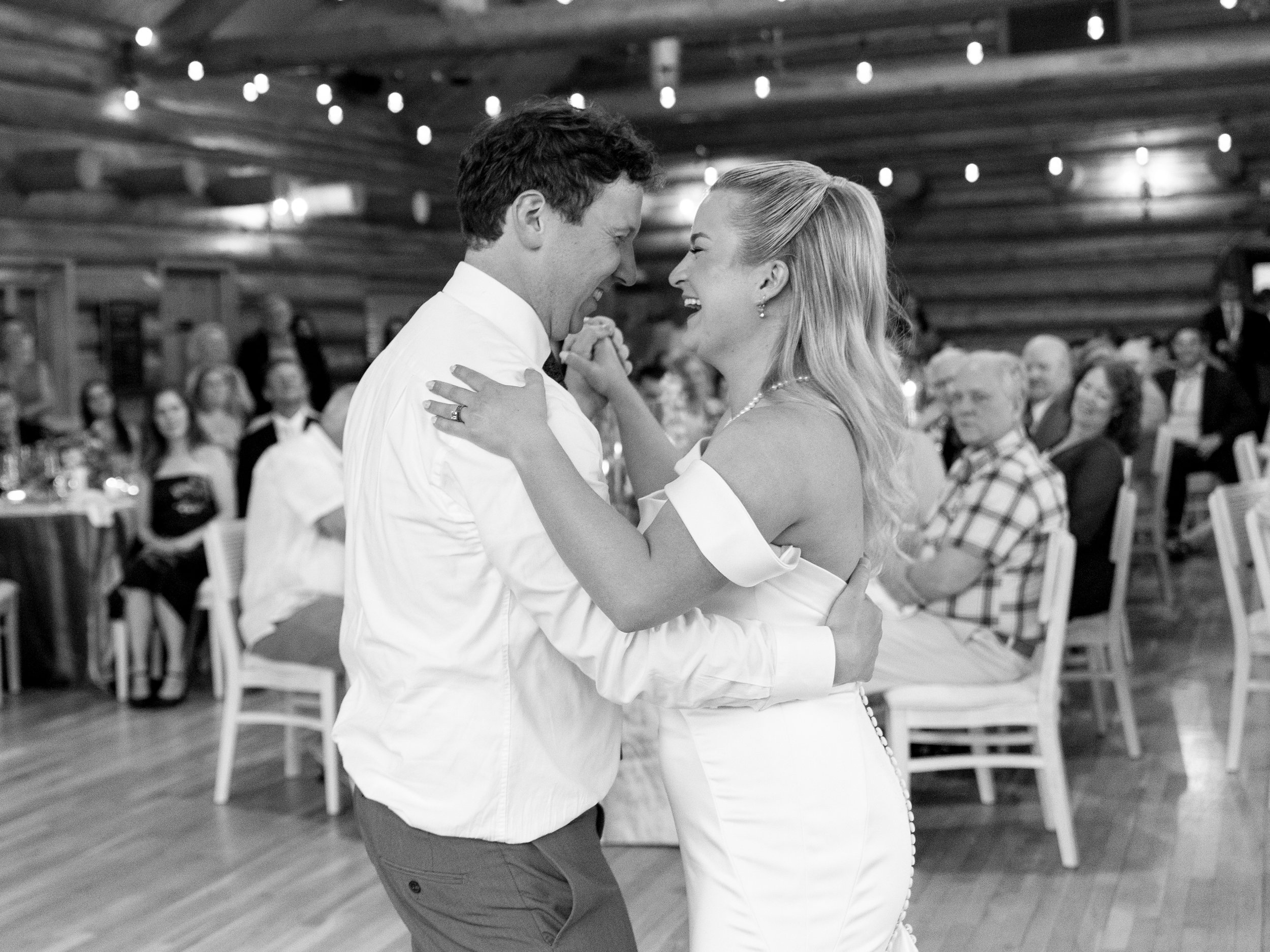 A bride and groom sharing their first dance at a wedding reception in a rustic venue with guests watching.
