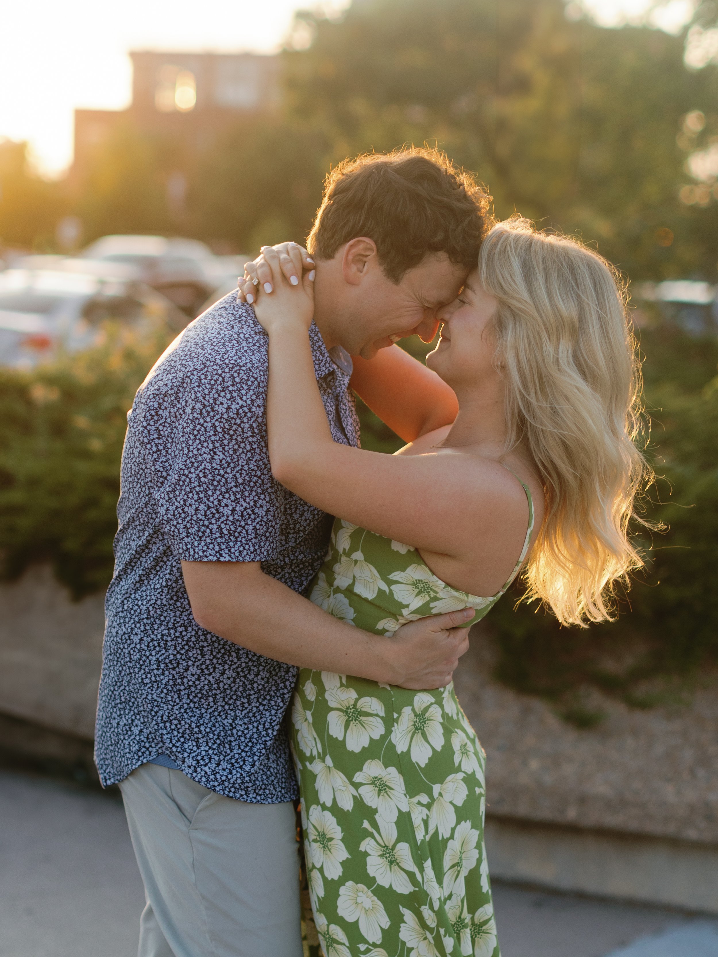 A couple embraces and touches foreheads at sunset, smiling and showing affection outdoors.