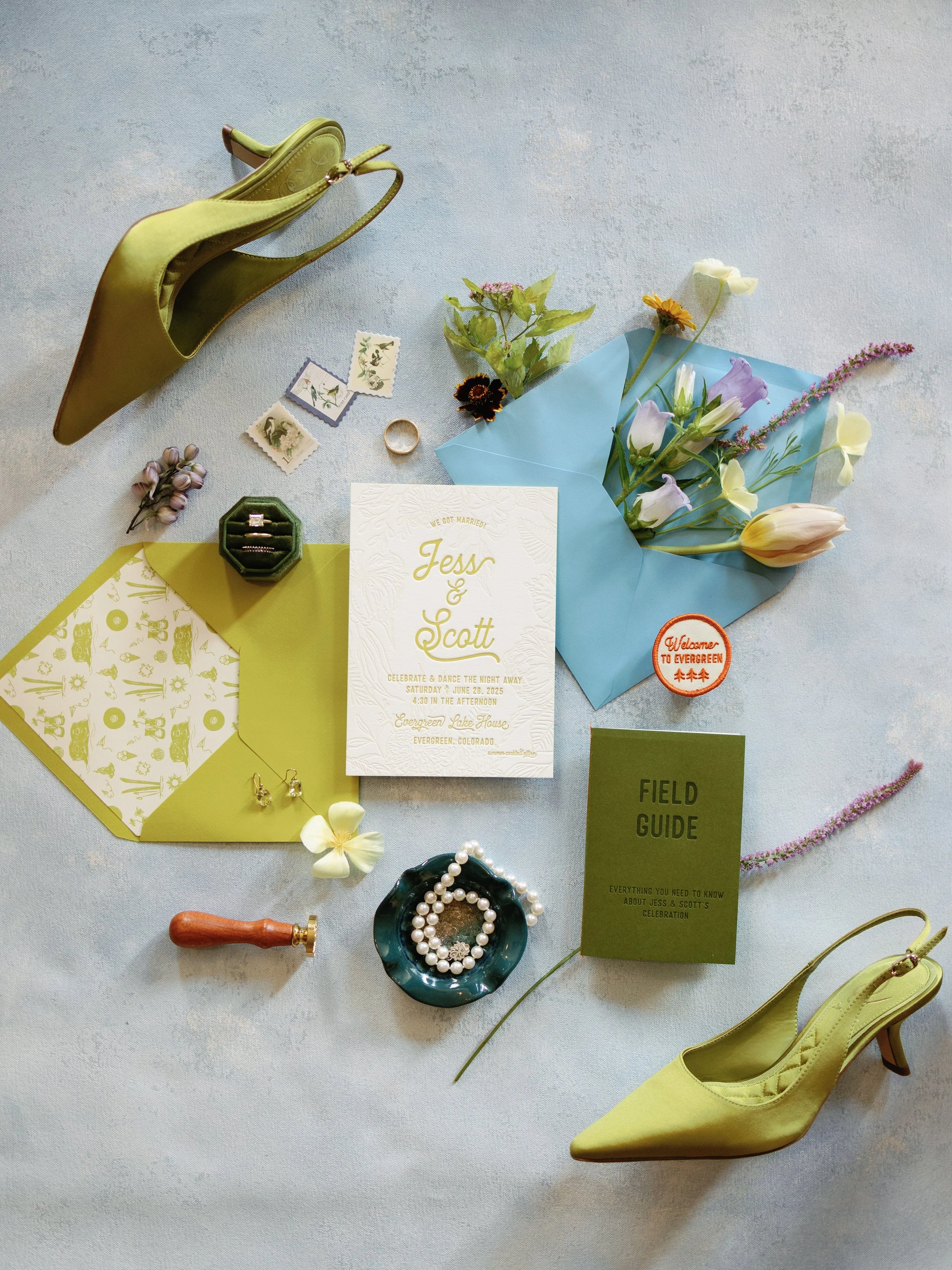 Wedding invitation, flowers, shoes, jewelry, and wedding accessories arranged on a light surface.