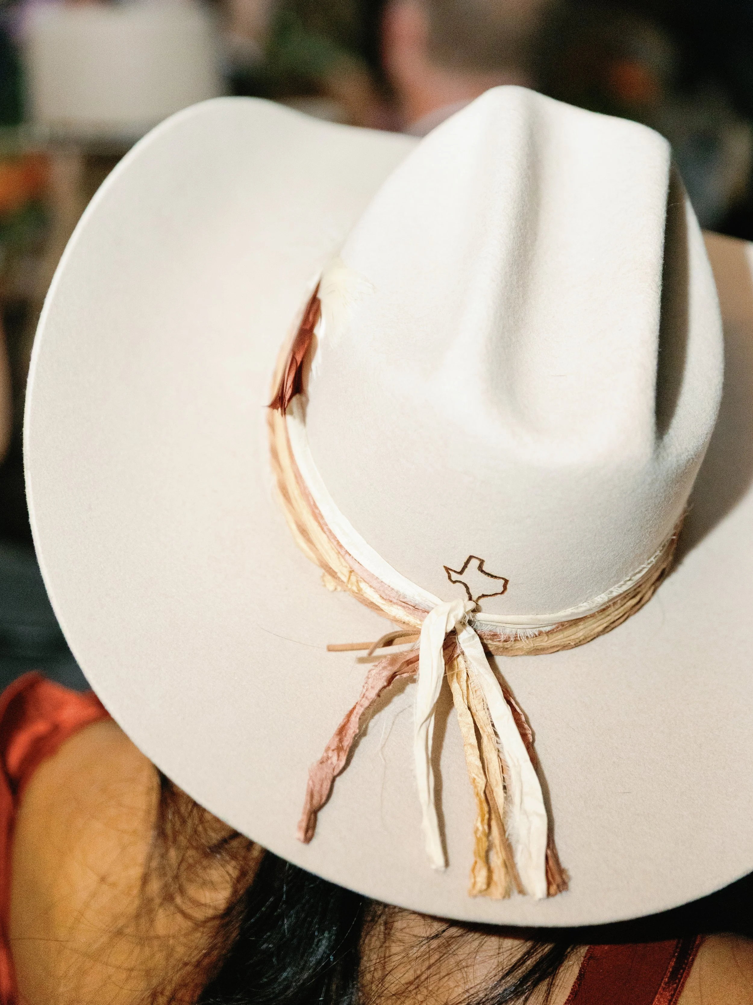 A white cowboy hat with a decorative band and a Texas-shaped pin.