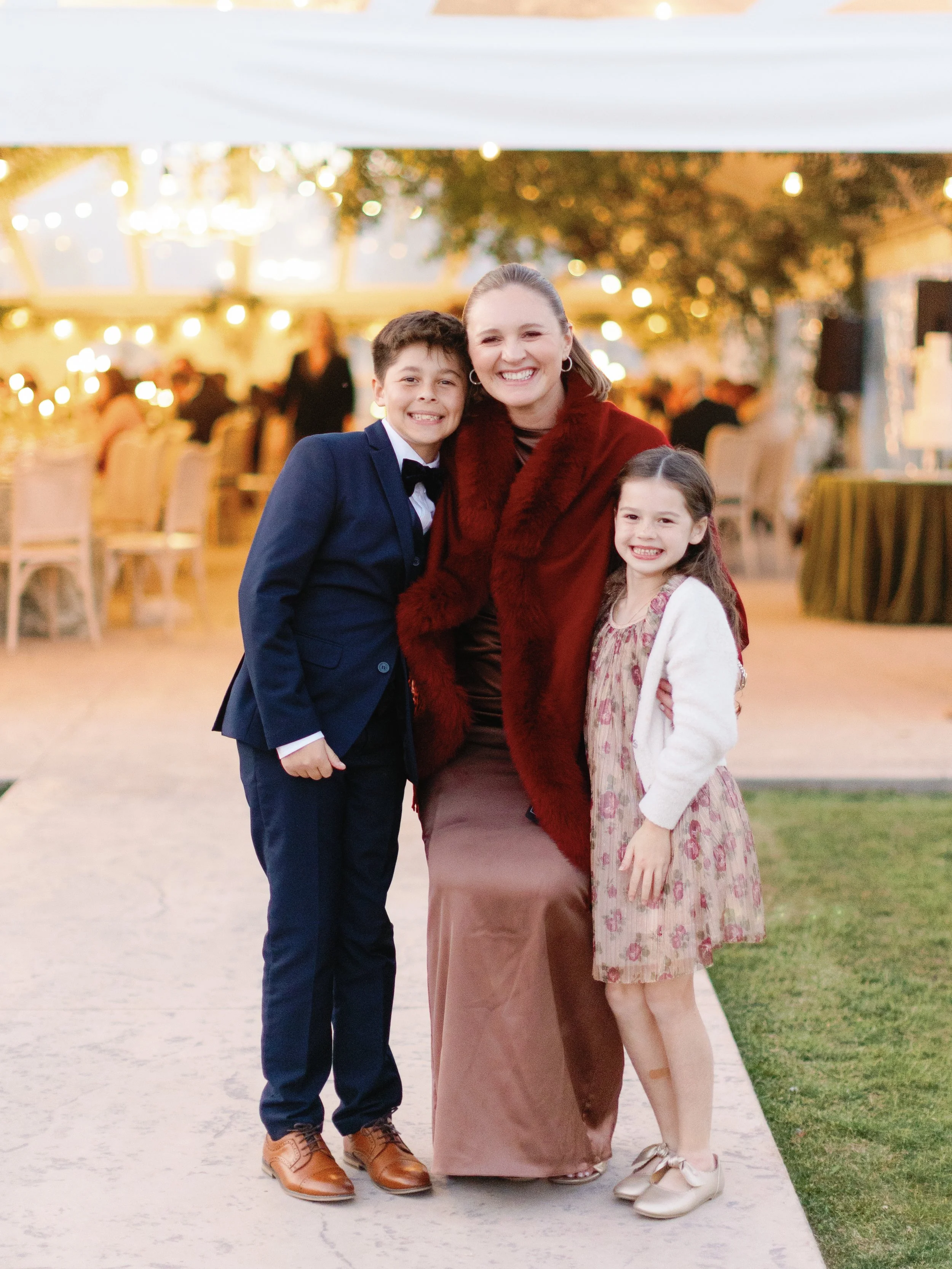 A woman and two children smiling at a celebration or party in a decorated indoor venue.