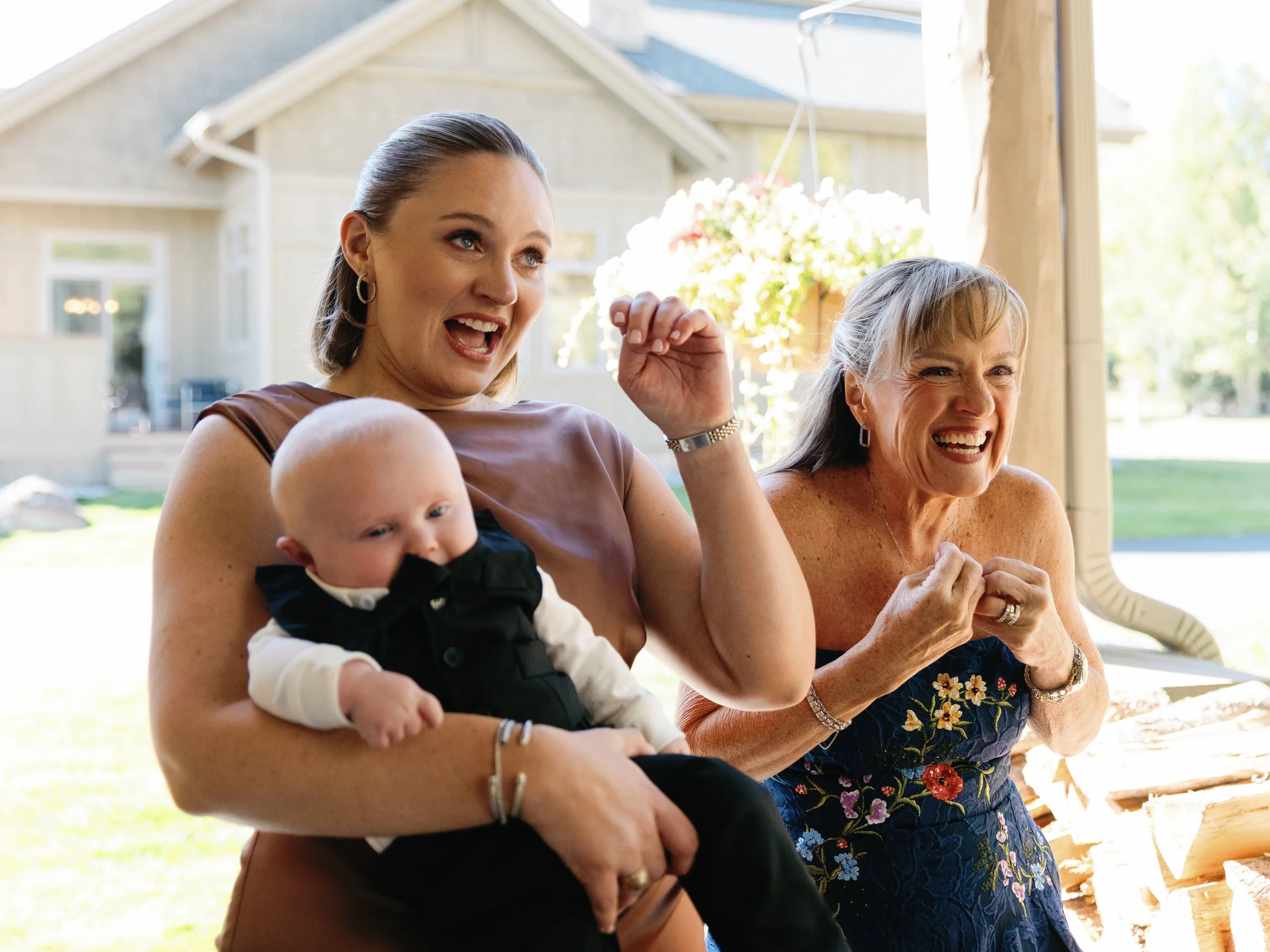 Two women and a baby enjoying a moment outdoors on a porch, laughing and smiling.