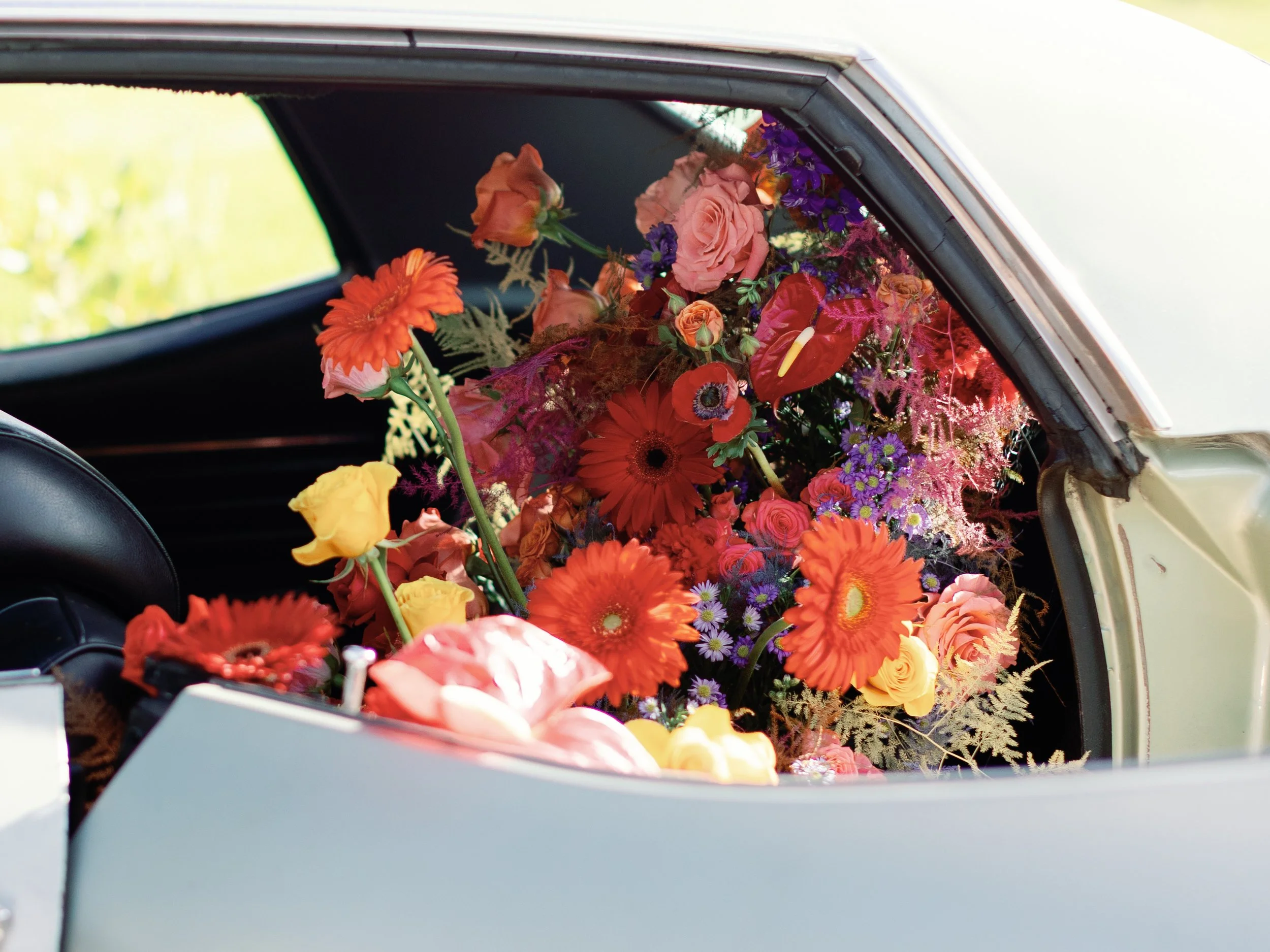 Colorful bouquet of various flowers including roses, daisies, and other blooms, placed inside a car's trunk or back area.