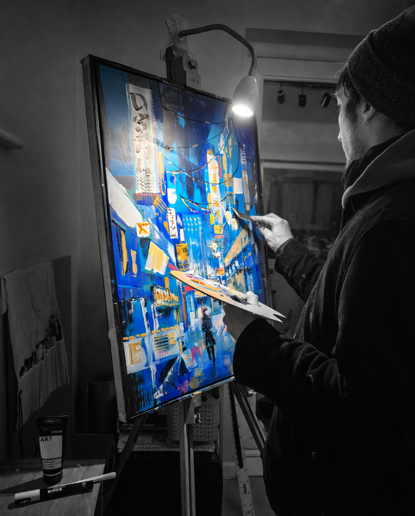 A person painting a colourful cityscape on a vertical canvas in a dimly lit indoor art studio.